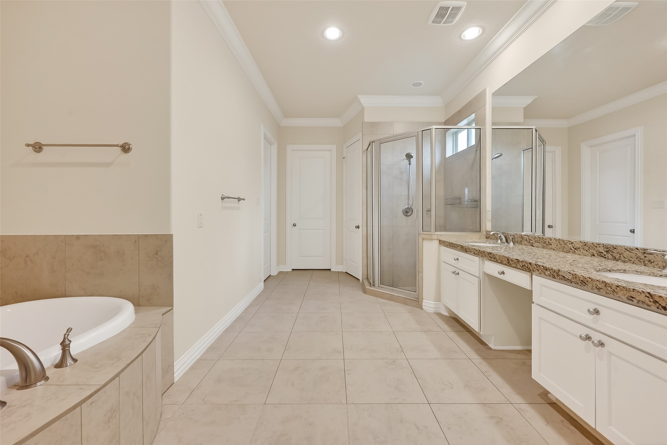 Primary bathroom offers two separate master closets, standing shower with clear enclosure, double vanities and an expansive wall mirror.