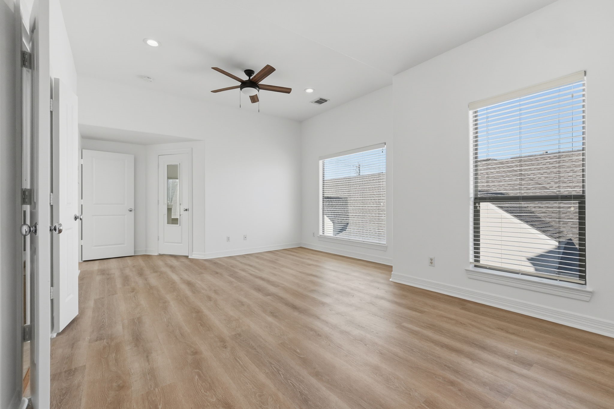 Another view of the primary bedroom highlights its expansive layout and multiple windows, complemented by a ceiling fan and neutral finishes for a bright, open feel. (3rd floor)