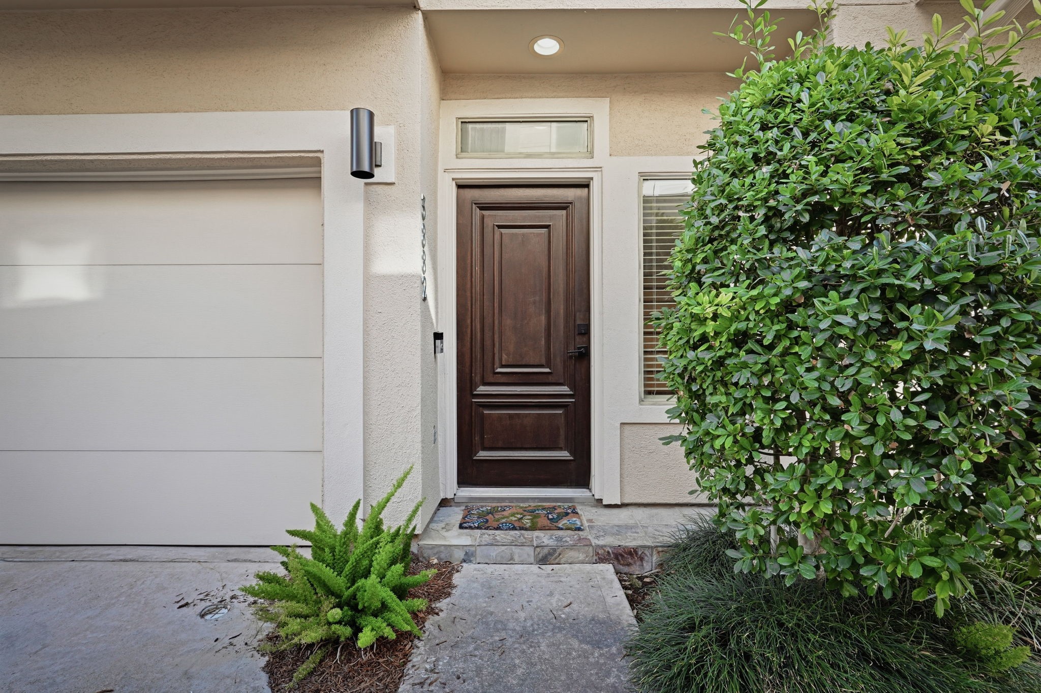 Welcoming front entry featuring a rich wood-paneled door, transom window, tiled porch, and manicured landscaping.