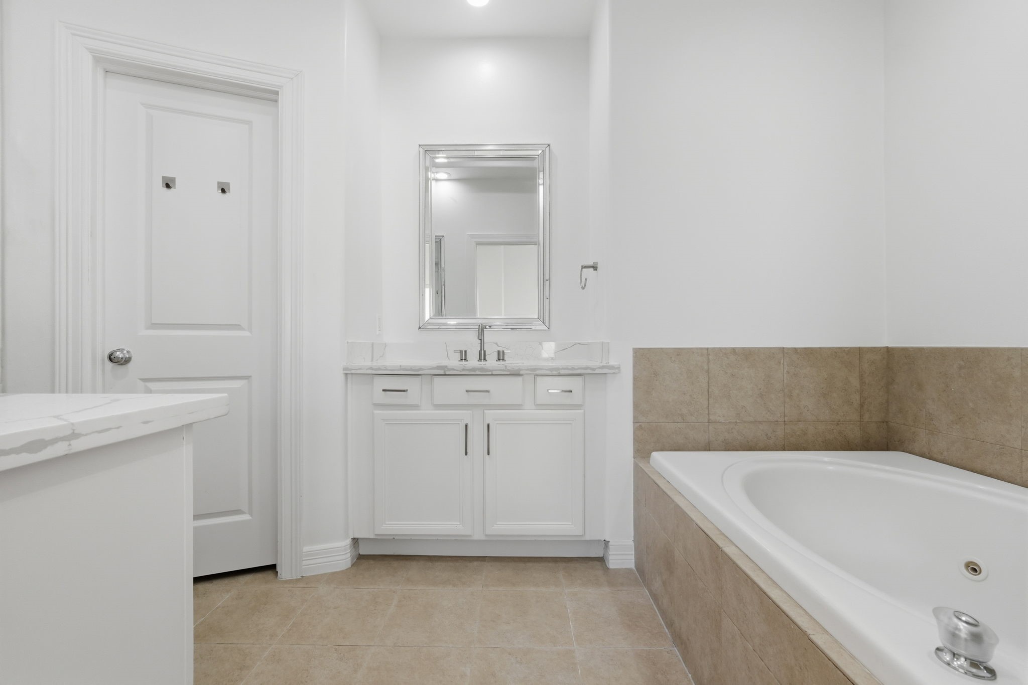 Another view of the primary bathroom features a jetted tub with a tiled surround, and a spacious vanity with generous counter space, combining refined finishes with added comfort and convenience. (3rd floor)