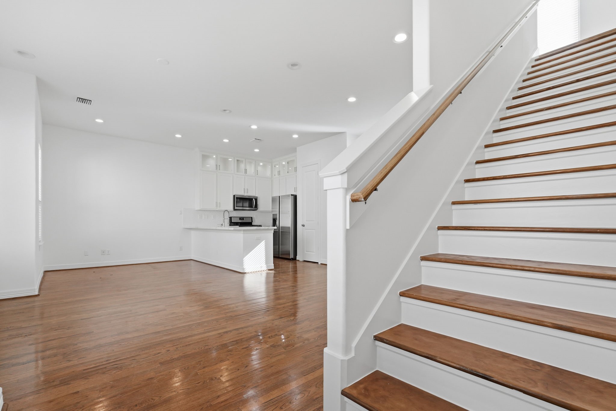 The staircase features rich wood treads, crisp white risers, and a coordinating handrail, creating a striking architectural detail alongside the open-concept living area and kitchen.