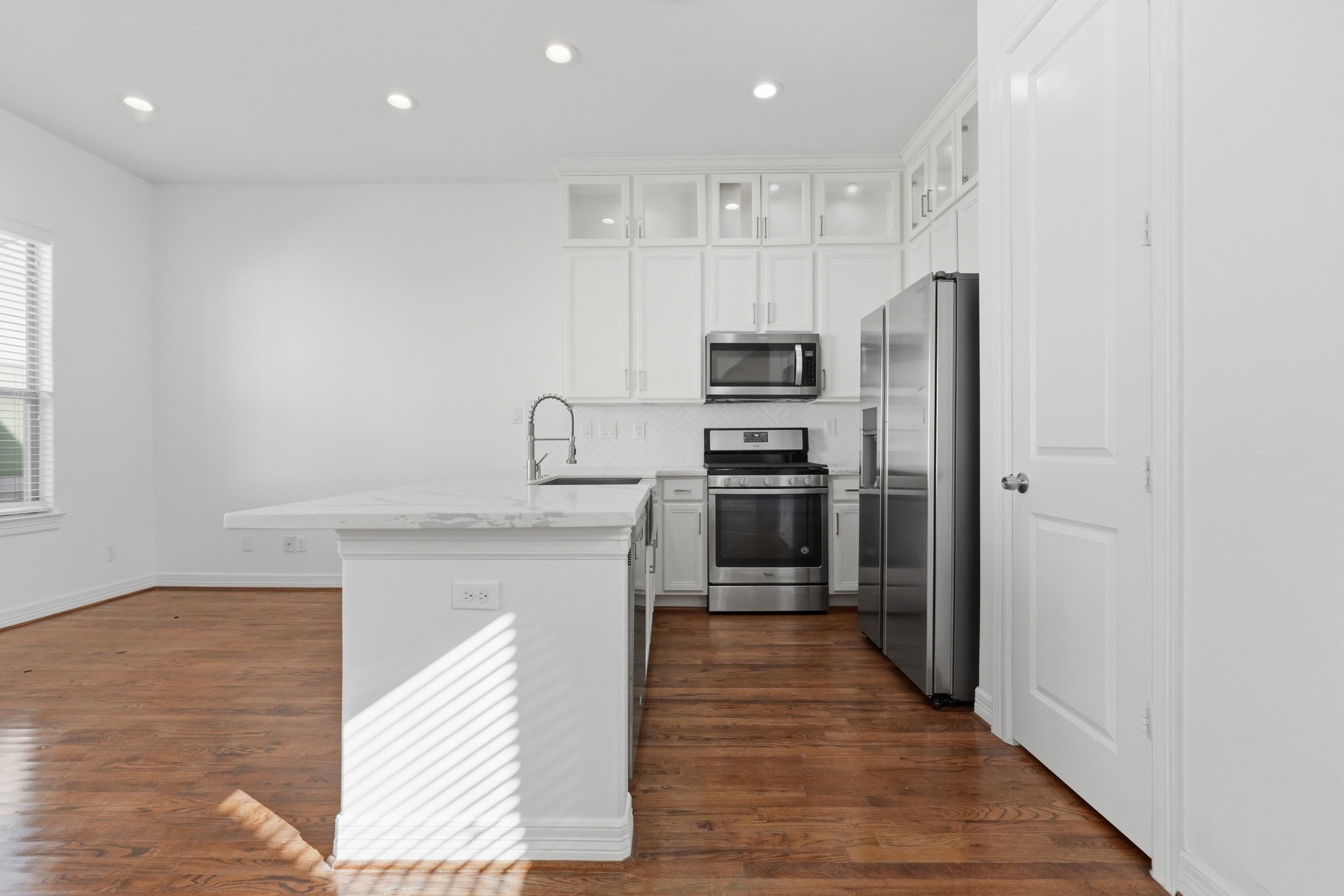 The kitchens clean-lined cabinetry, stainless steel appliances, and extended breakfast bar create a functional workspace, while the open layout provides an easy transition into the dining and main living area.