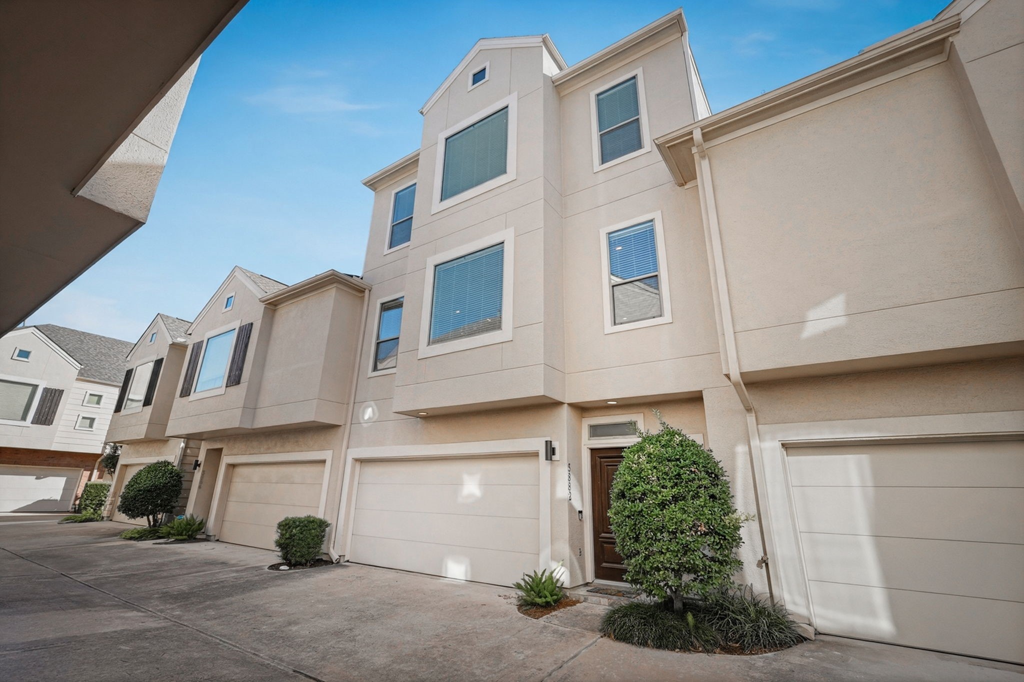 Attractive three-story townhome featuring a stucco exterior, attached garage, and landscaped front entry in a courtyard-style community