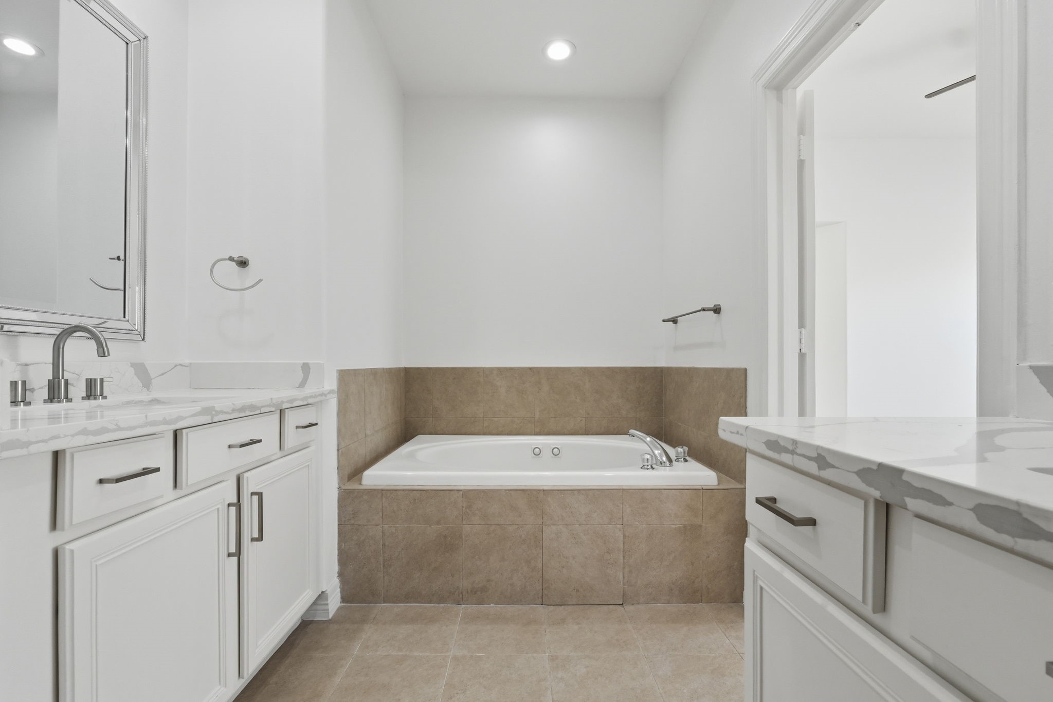 The primary bathrooms jetted tub takes center stage, featuring a tiled surround and positioned between the dual vanities for a well-appointed and functional layout.