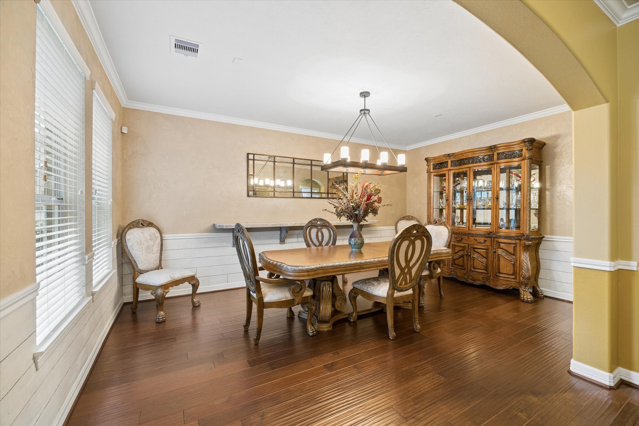 An elegant formal dining room offers a refined setting for memorable gatherings, featuring rich hardwood floors, crown molding, abundant natural light, a stylish faux accent wall, and timeless architectural details that enhance its sophisticated appeal.