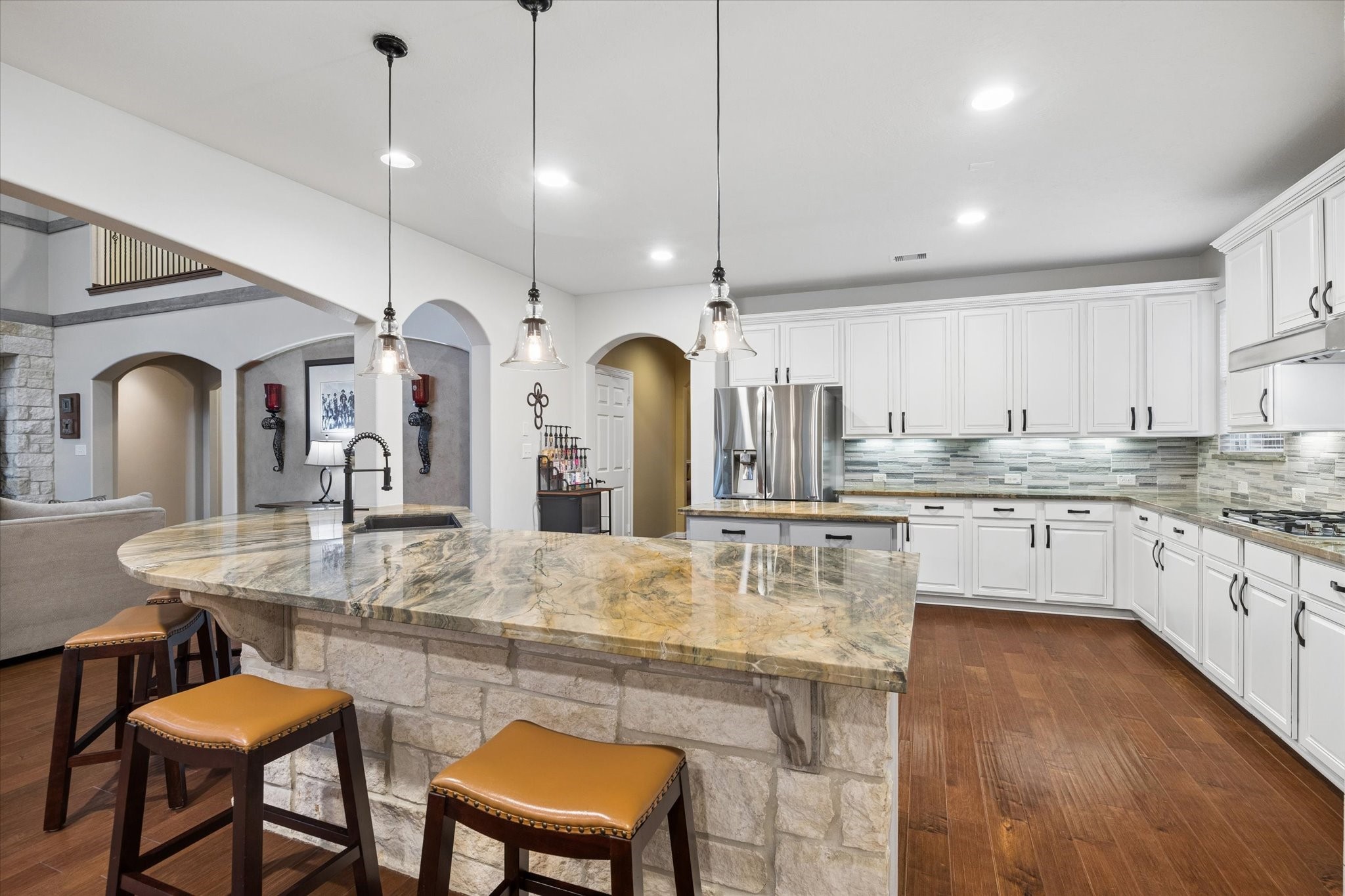 Designed for gathering and entertaining, the expansive kitchen features a generous breakfast bar with seating, beautiful stone accents, abundant cabinetry, and extensive counter space. Pendant lighting adds warmth and character, while the open design creates a natural connection to the family room.