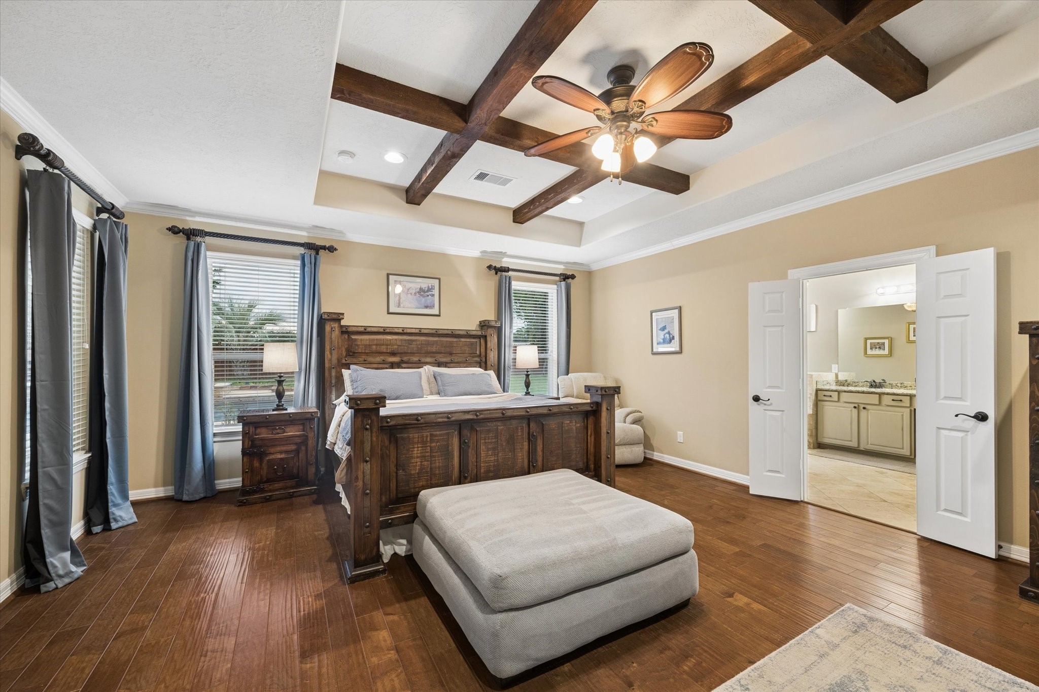 The generously sized primary suite offers a warm and inviting retreat, highlighted by beautiful wood flooring, abundant natural light, and a distinctive tray ceiling accented with exposed wood beams. Double doors provide a gracious entrance to the en-suite bath, completing this comfortable and private space.