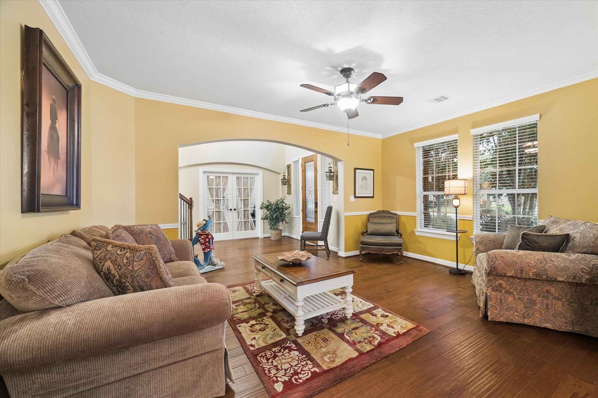 Another perspective of the spacious living room highlights its warm and inviting atmosphere, with rich hardwood floors, crown molding, and abundant natural light. The generous layout offers plenty of space to relax, gather, and enjoy everyday living.