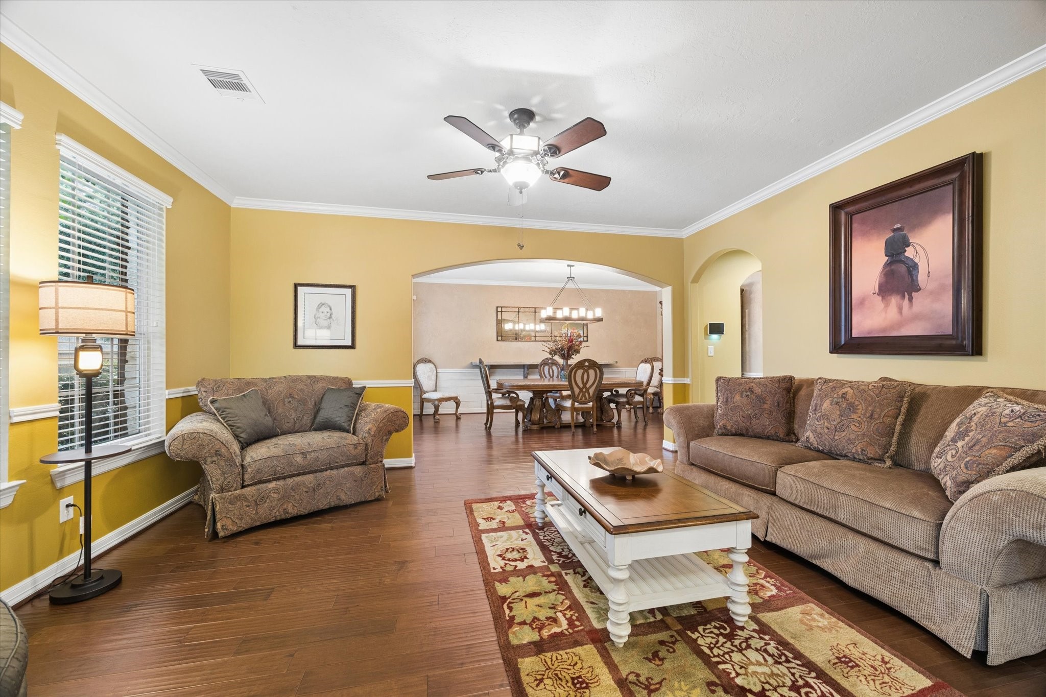 A spacious living area flows seamlessly into the formal dining room, creating an inviting setting for both everyday living and entertaining. Rich hardwood floors, crown molding, and abundant natural light enhance the warmth and character of the space.