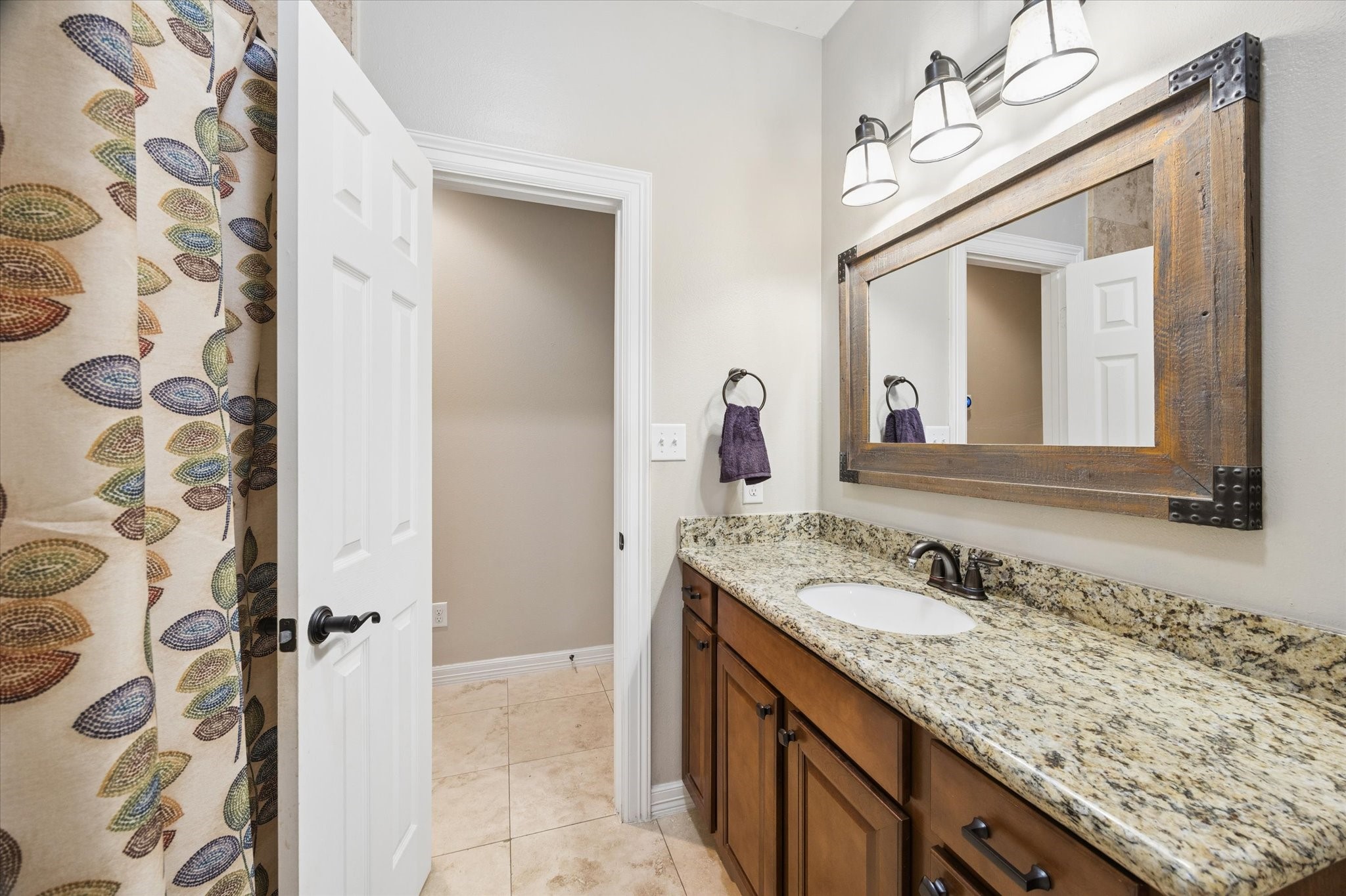A well-appointed secondary bathroom on the first floor features a granite countertop, warm wood cabinetry, and a practical layout, offering comfort and convenience for family members or guests.