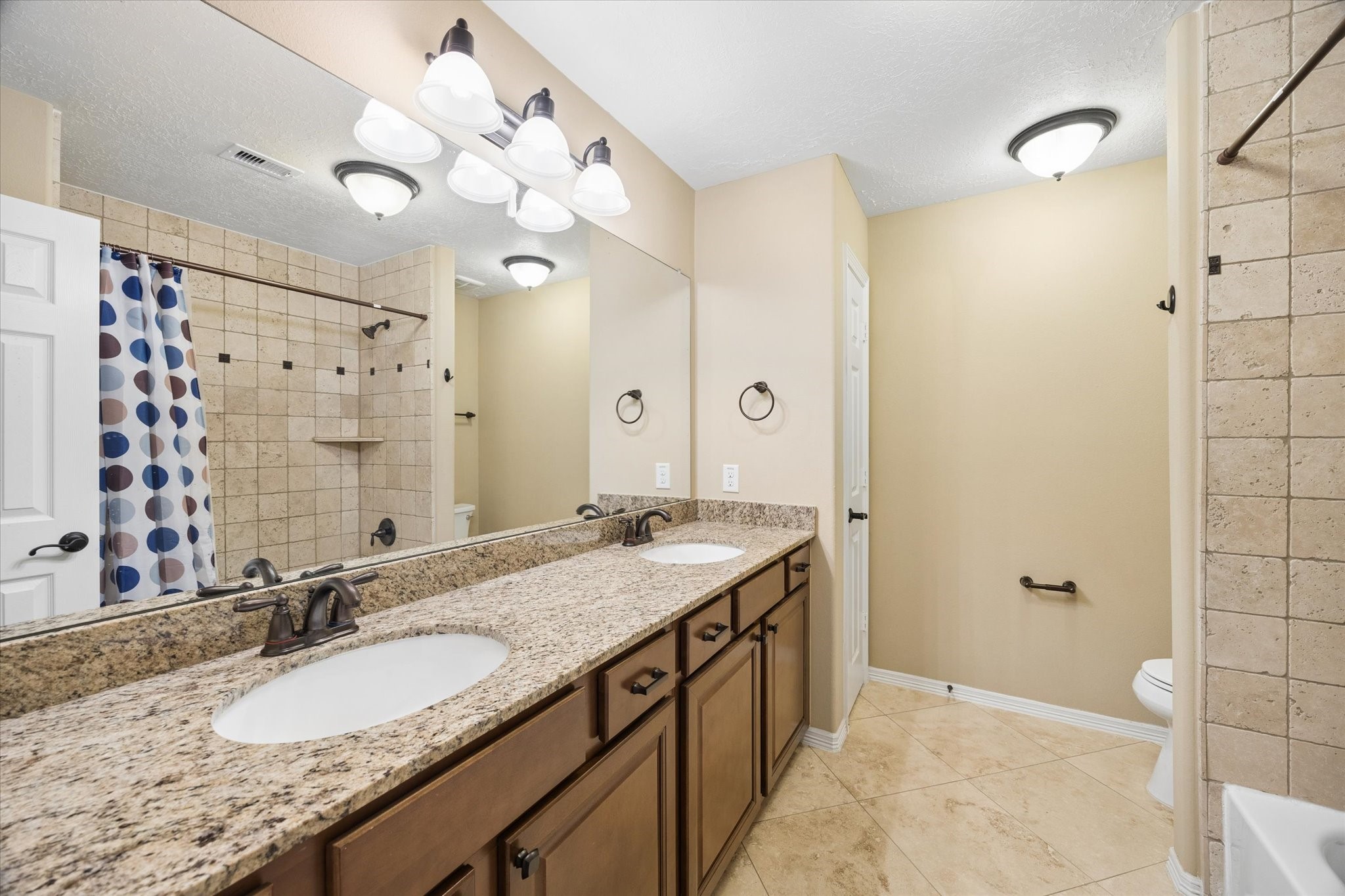 Well-appointed upstairs secondary bathroom featuring an expansive granite countertop, dual sinks, abundant cabinetry, LED lighting, and a tiled tub and shower combination.