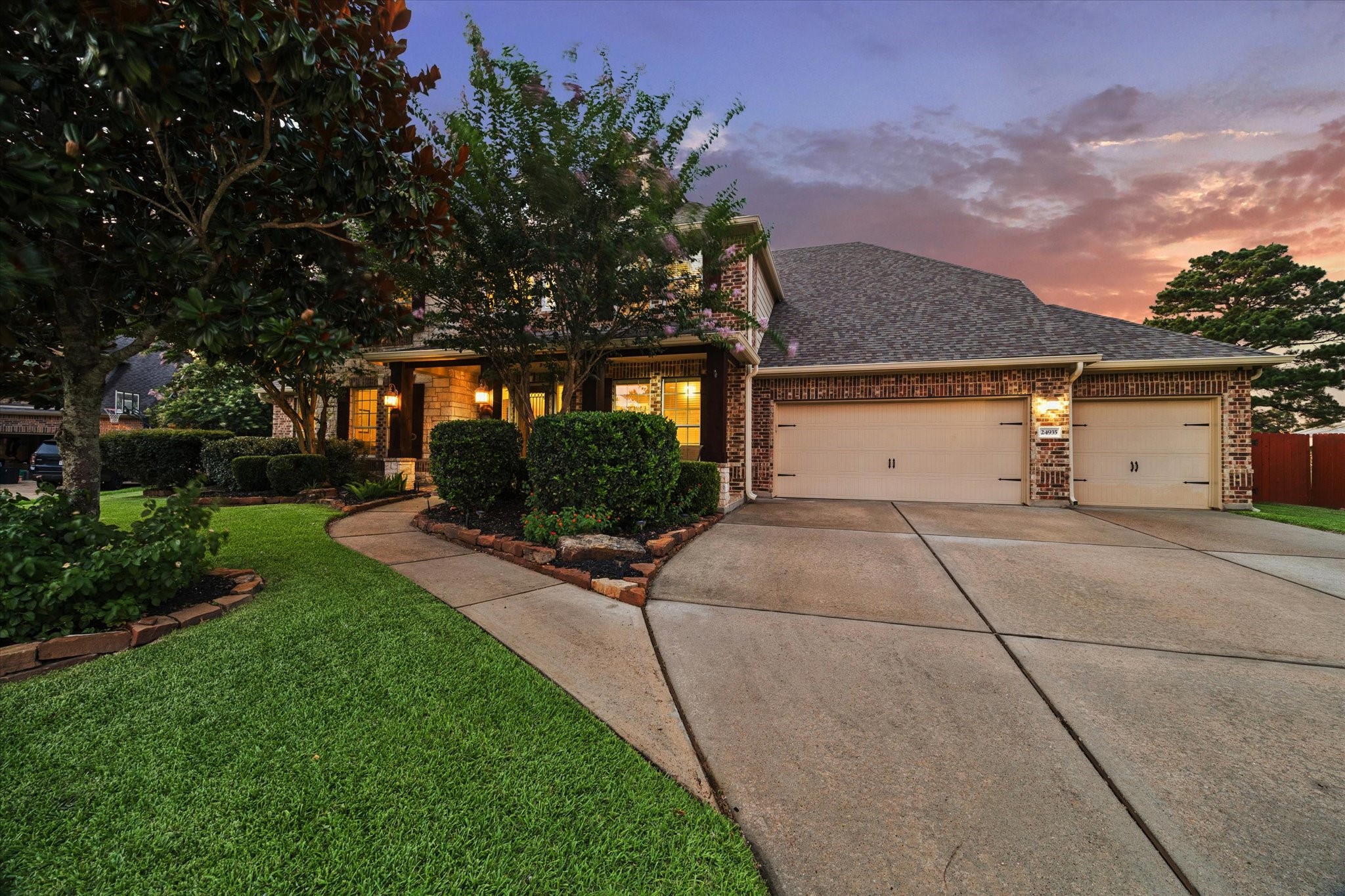 A spacious driveway leads to the three-car garage and welcoming front entrance, beautifully framed by lush landscaping and the homes timeless architectural details.