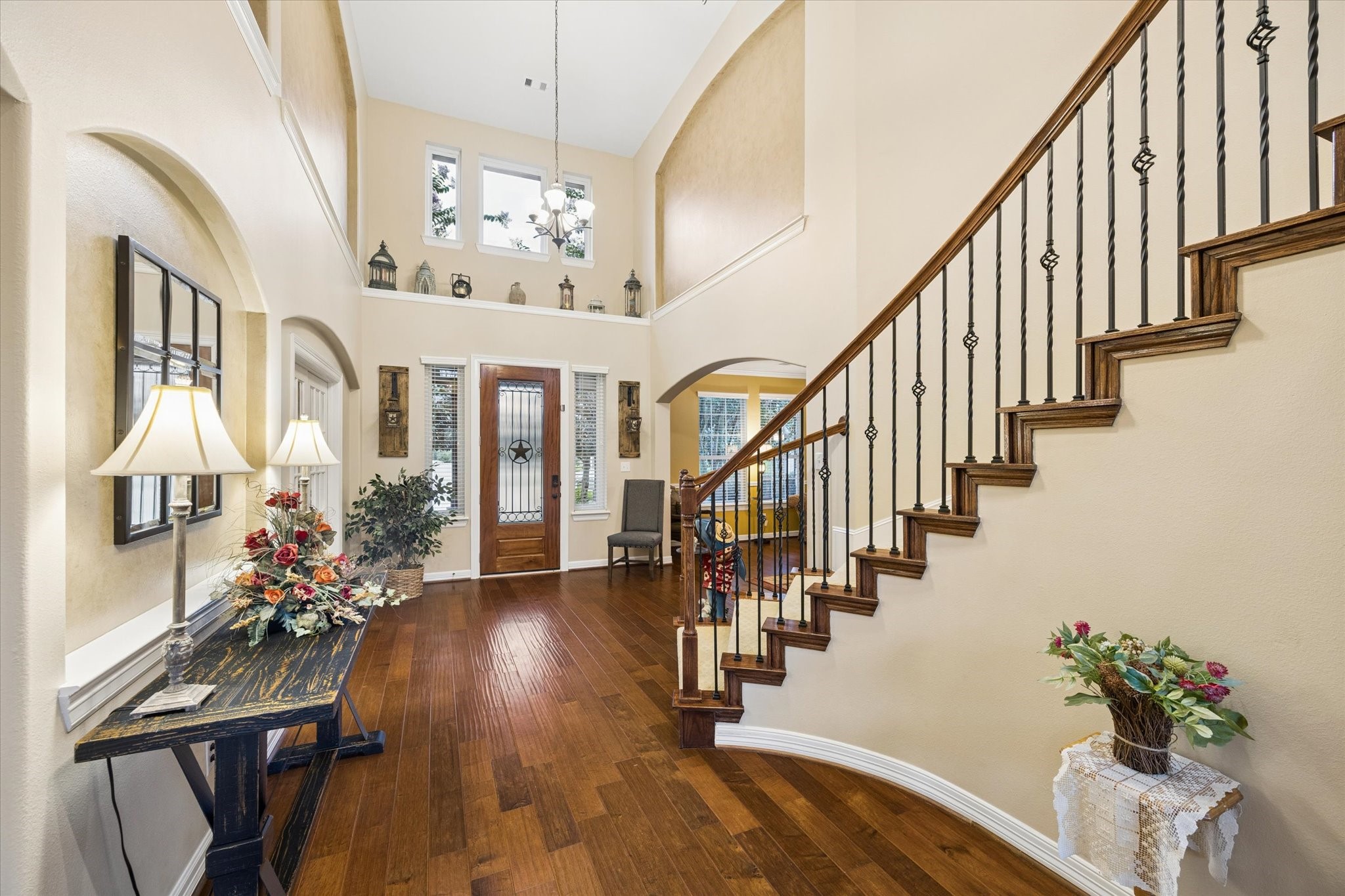 A different perspective of the grand entry highlights the soaring ceilings, rich hardwood floors, and elegant staircase with wrought-iron details. Abundant natural light enhances the open and welcoming design, setting the tone for the impressive spaces throughout the home.