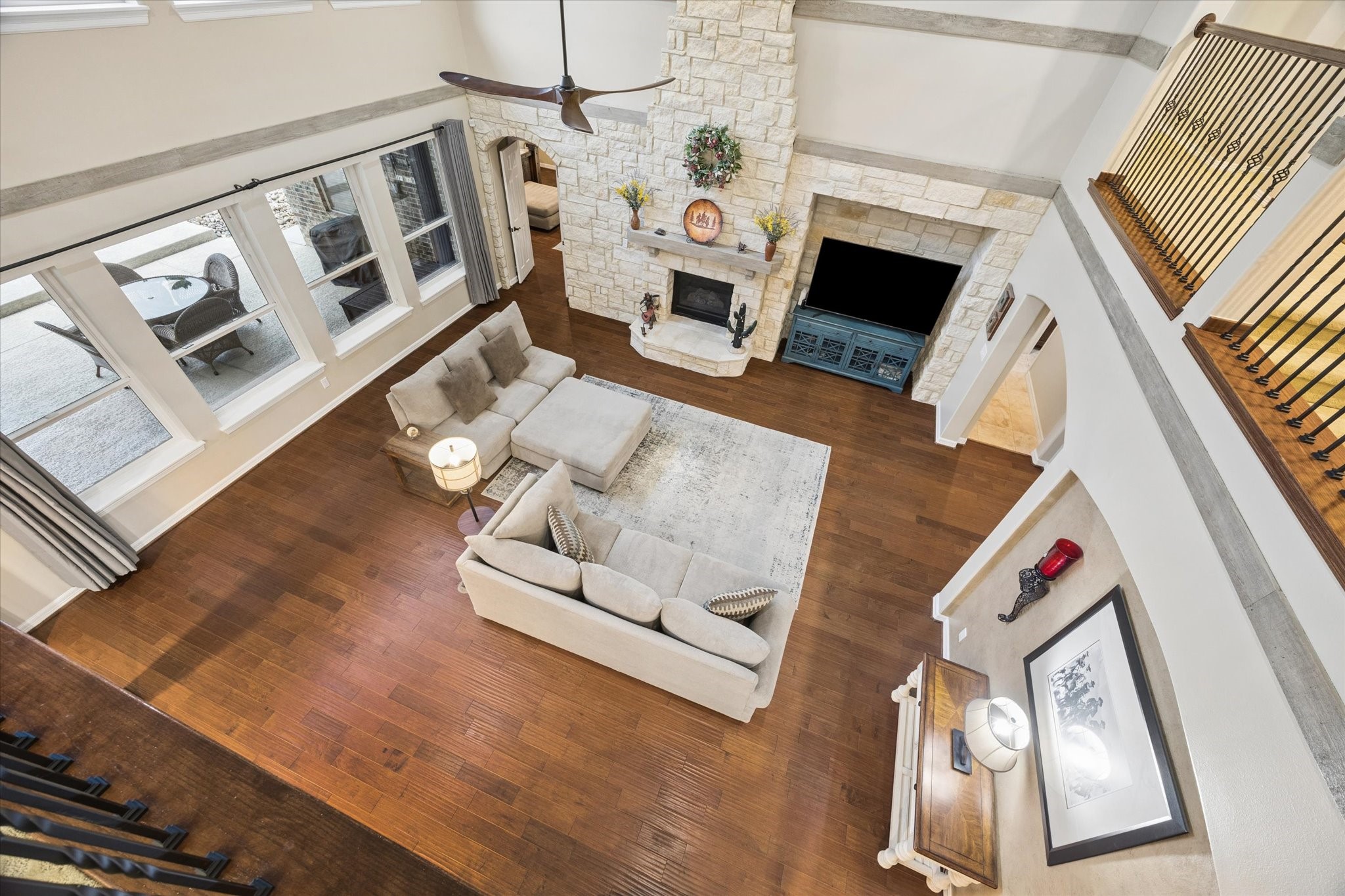 An impressive view from the second level overlooks the expansive family room, showcasing the homes soaring ceilings, beautiful wood flooring, striking stone fireplace, and abundant natural light. The open design and architectural details create a remarkable sense of space and connection throughout the home.