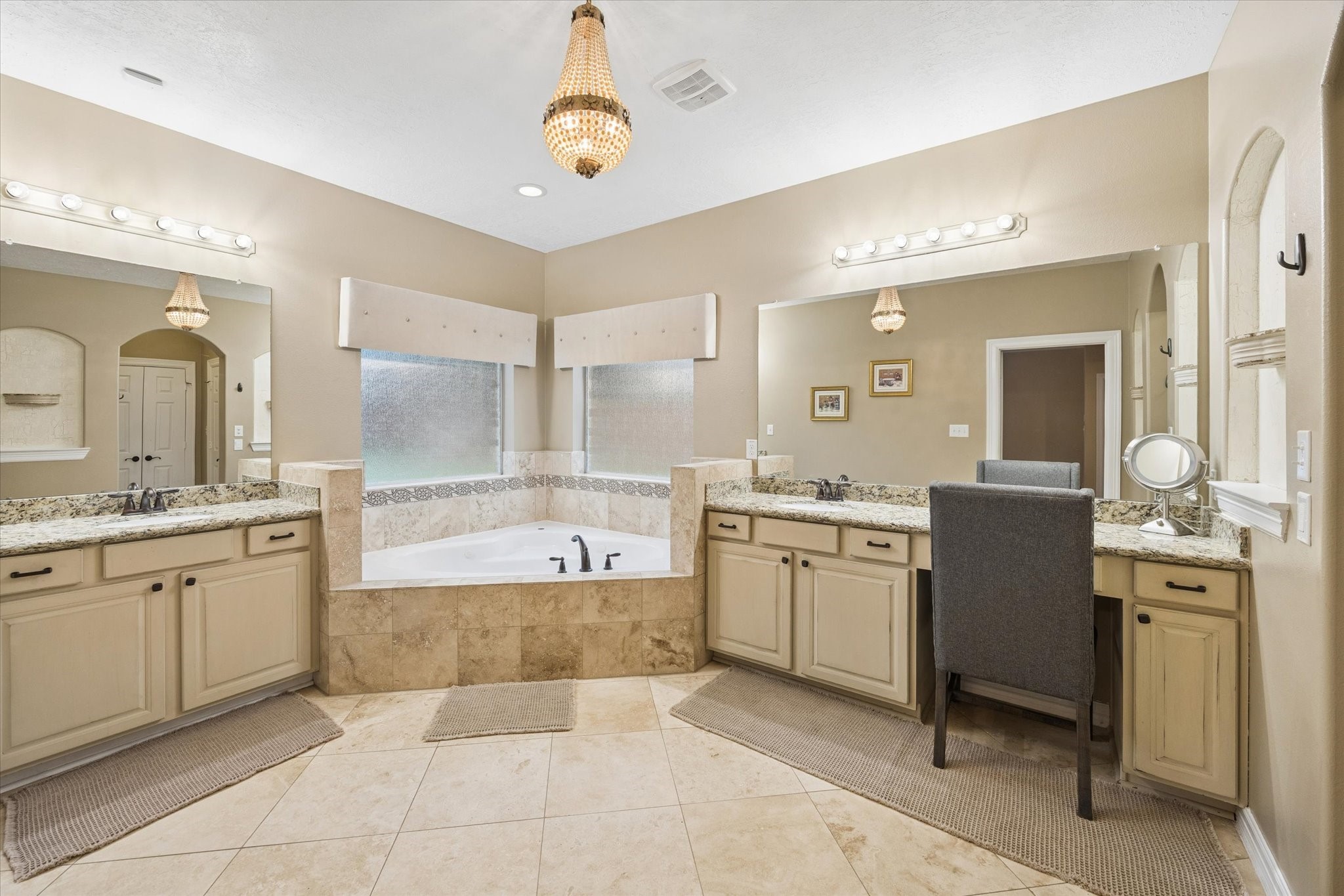 The primary en-suite bath offers a relaxing retreat with dual vanities, granite countertops, abundant cabinetry, and a large jetted soaking tub surrounded by tile. Generous proportions and thoughtful design create a comfortable and functional space for everyday living.
