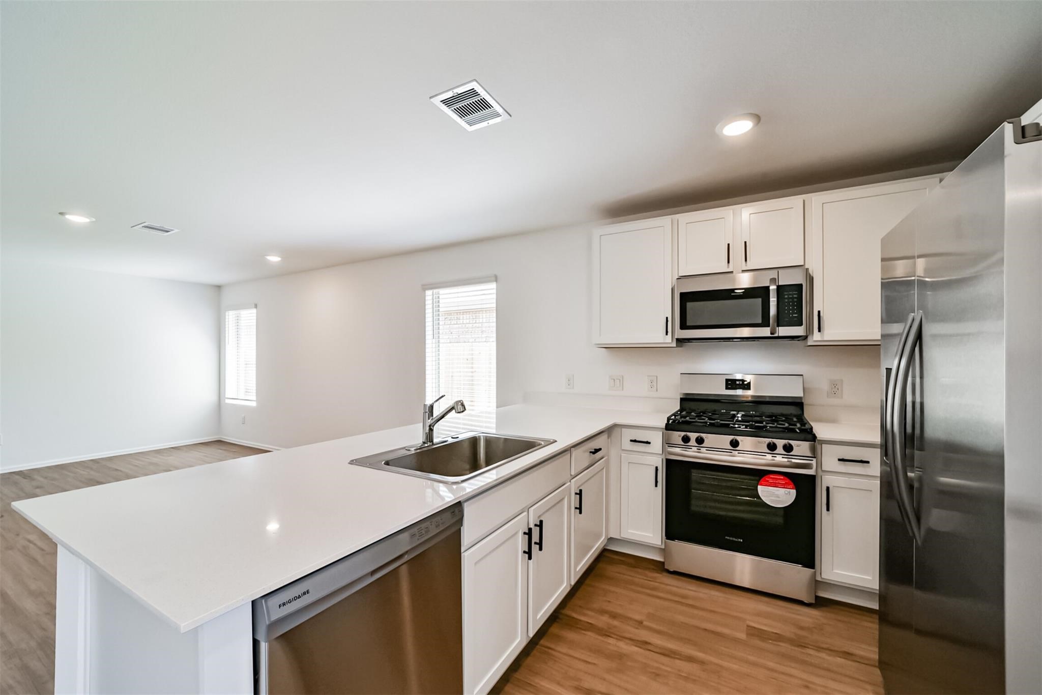 Open-concept family room with abundant natural light, seamlessly connecting to the beautiful kitchen featuring white cabinets with black handles and stainless steel appliances
