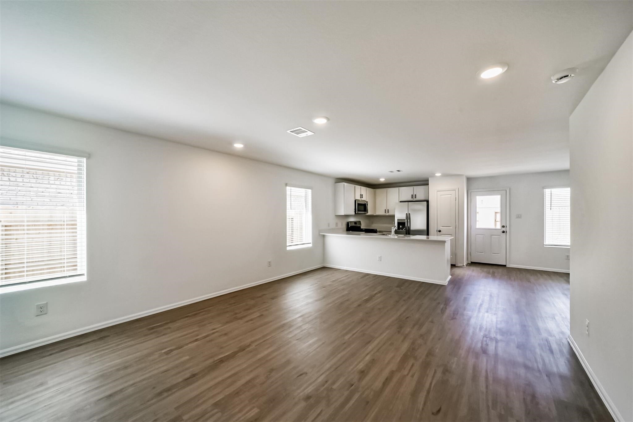 Open concept family room with abundant natural light, seamlessly connecting to the beautiful kitchen featuring white cabinets with black handles and stainless steel appliances.