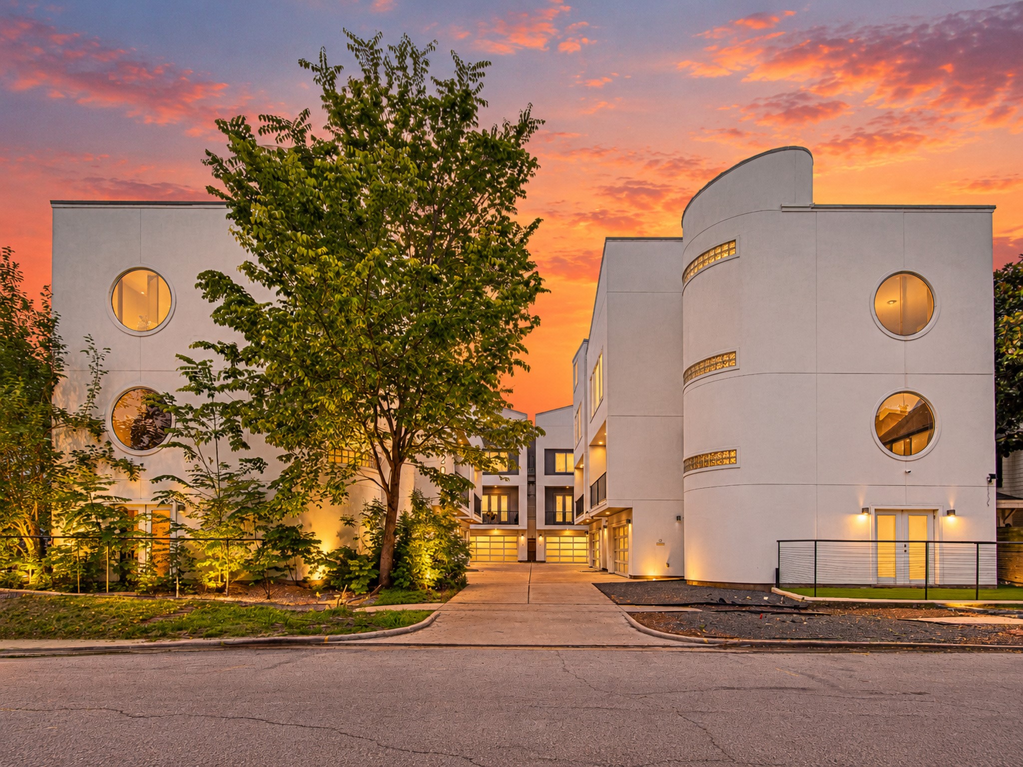 Contemporary exterior featuring distinctive curved walls, circular windows, and mature landscaping at sunset.