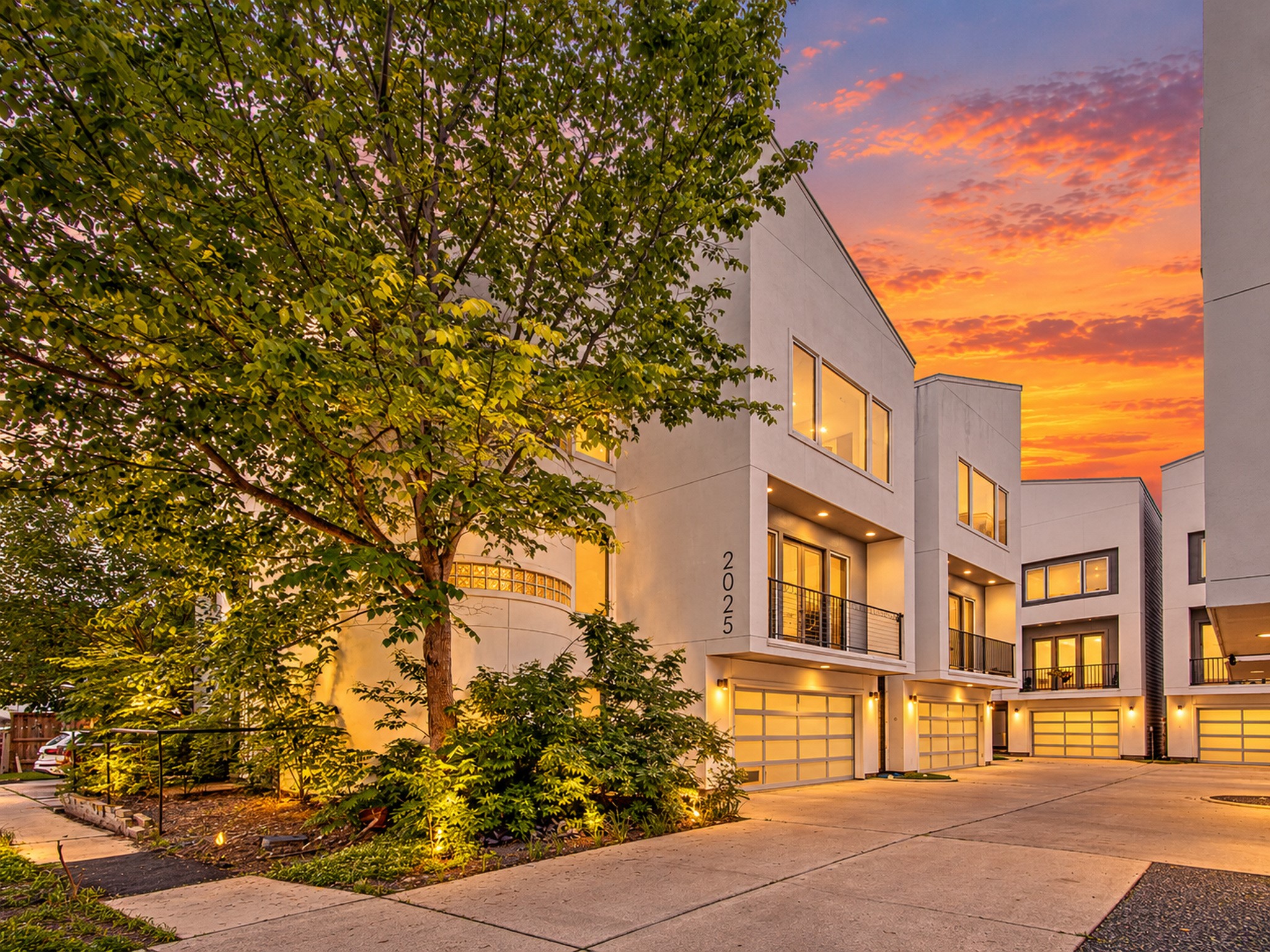 Mature trees and landscaped beds frame the approach to the home and its attached garage.