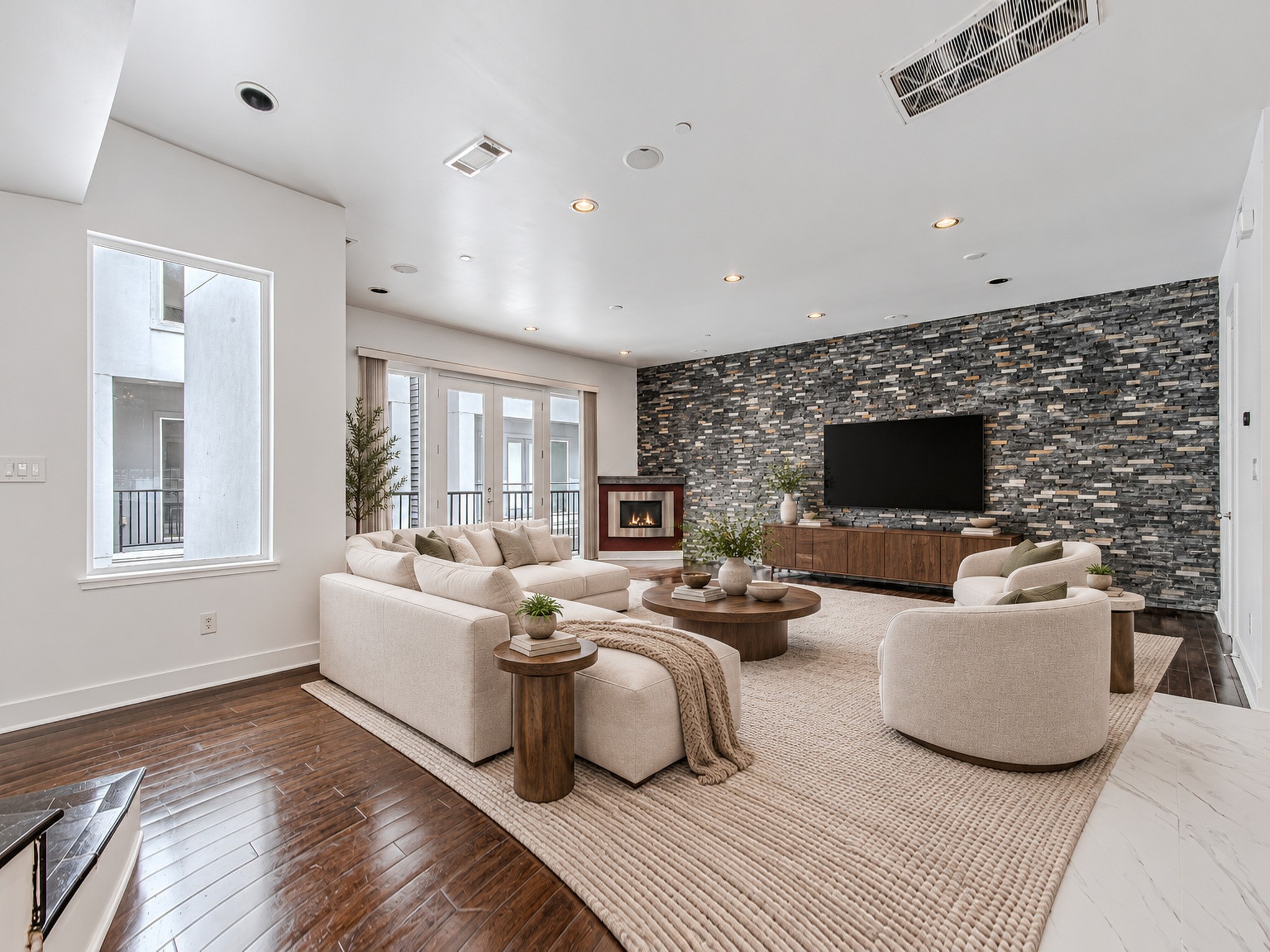 Spacious living room featuring a textured accent wall, dark wood flooring, and abundant natural light.