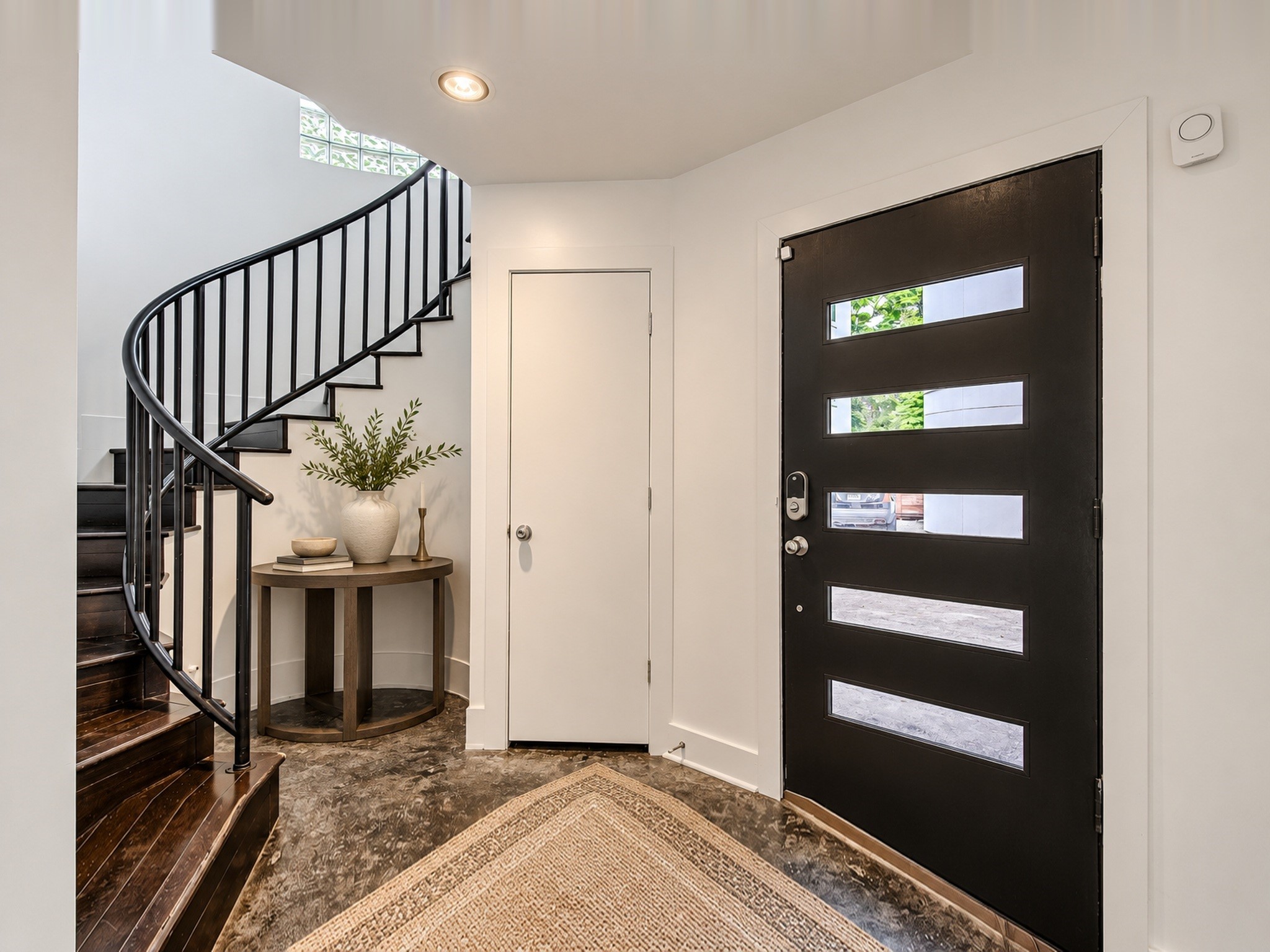 Welcoming entry featuring a modern glass-paneled door, patterned flooring, and a dramatic curved staircase.