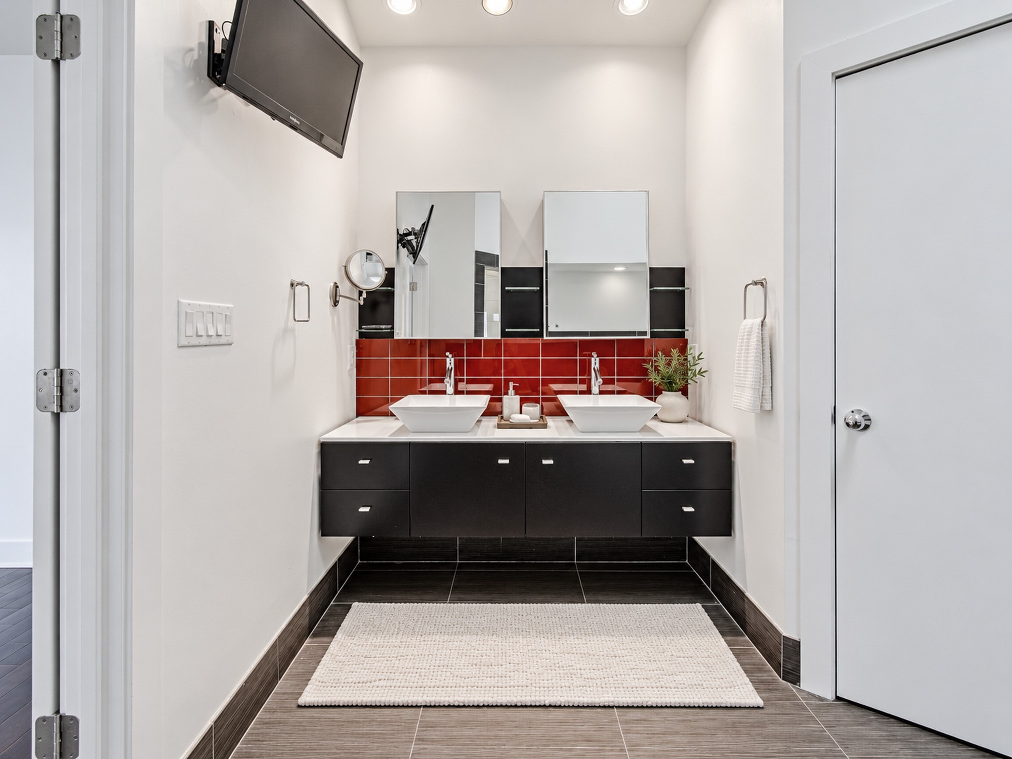 Additional view of the primary bathroom highlighting its floating vanity, mirrored storage, and contrasting finishes.