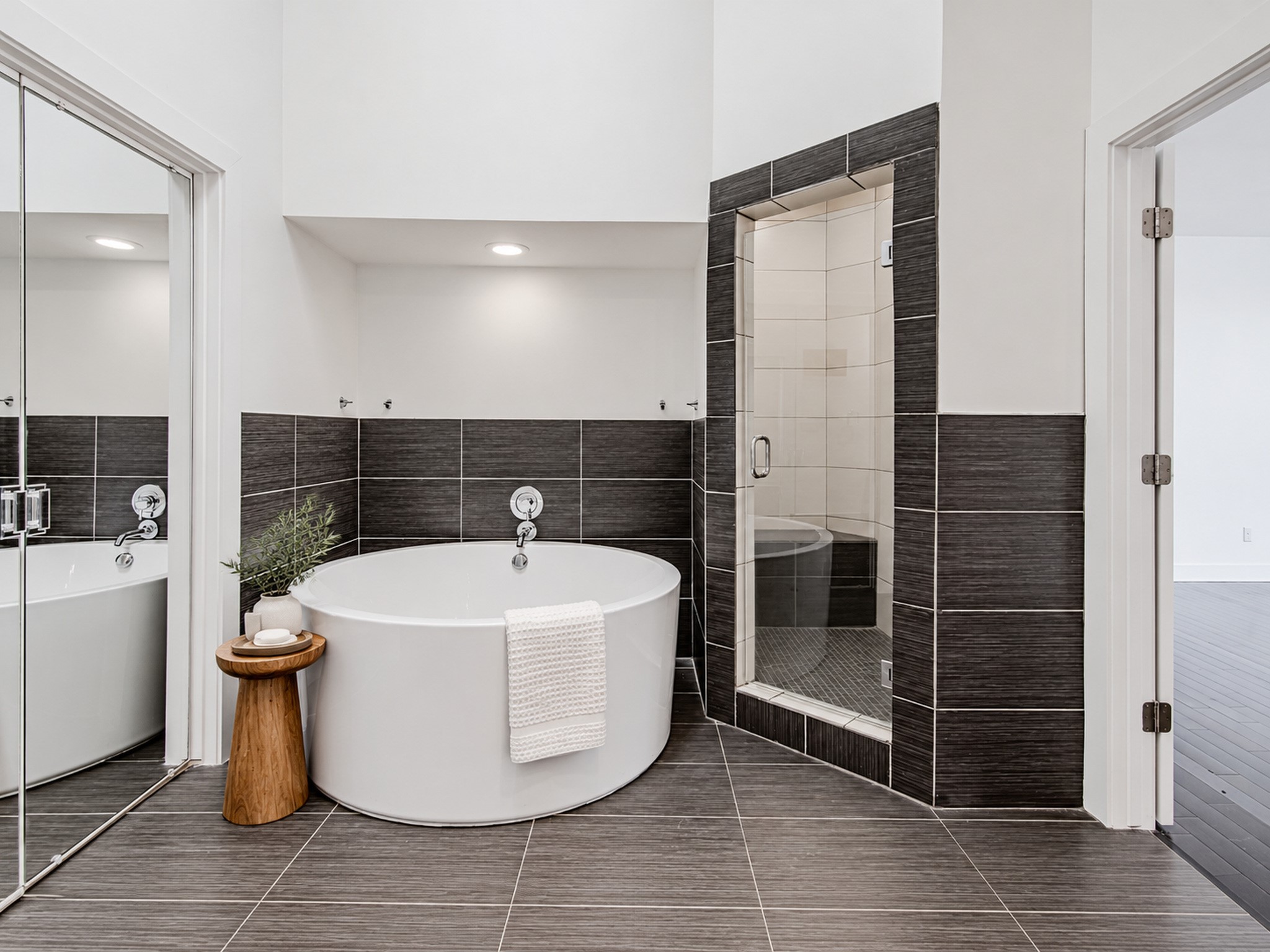 Primary bathing area featuring a freestanding soaking tub, separate glass-enclosed shower, and dark tile accents.