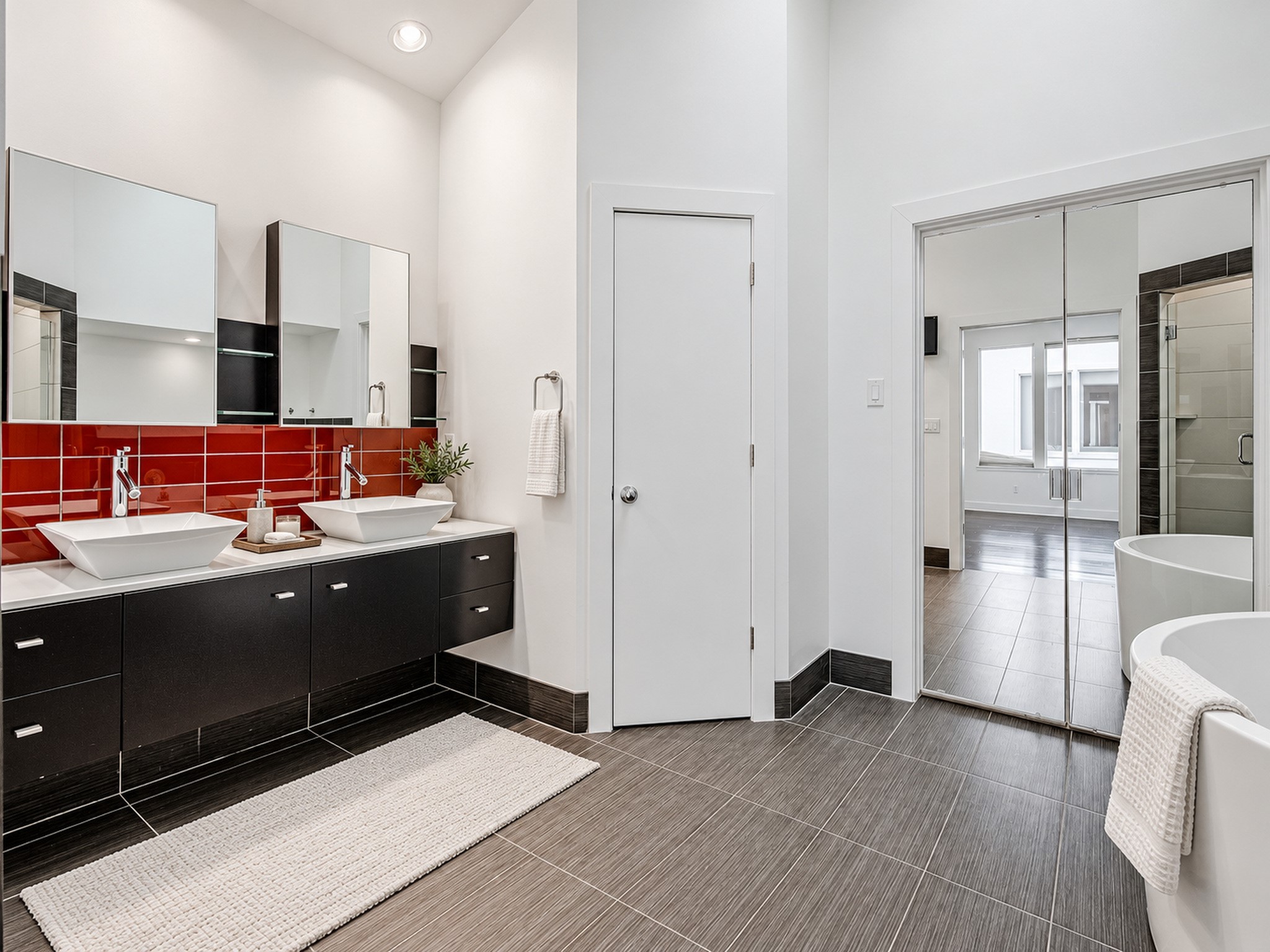 Primary bathroom featuring dual sinks, dark vanity cabinetry, a bold red backsplash, and a separate tub and shower area.