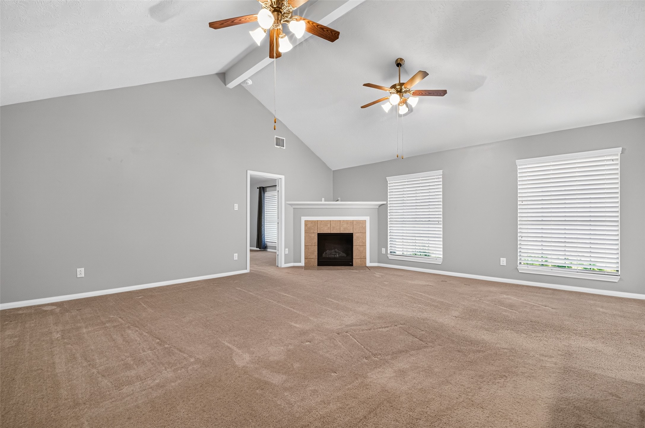 Living room features a high vaulted ceiling, two ceiling fans, a tile-surround fireplace, and windows that bring in natural light.