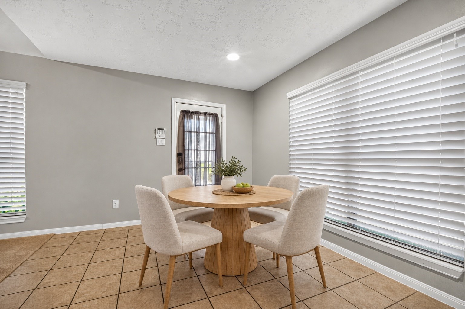 Additional view of the virtually staged breakfast area highlights windows on two walls, tile flooring, recessed lighting, and an exterior door.