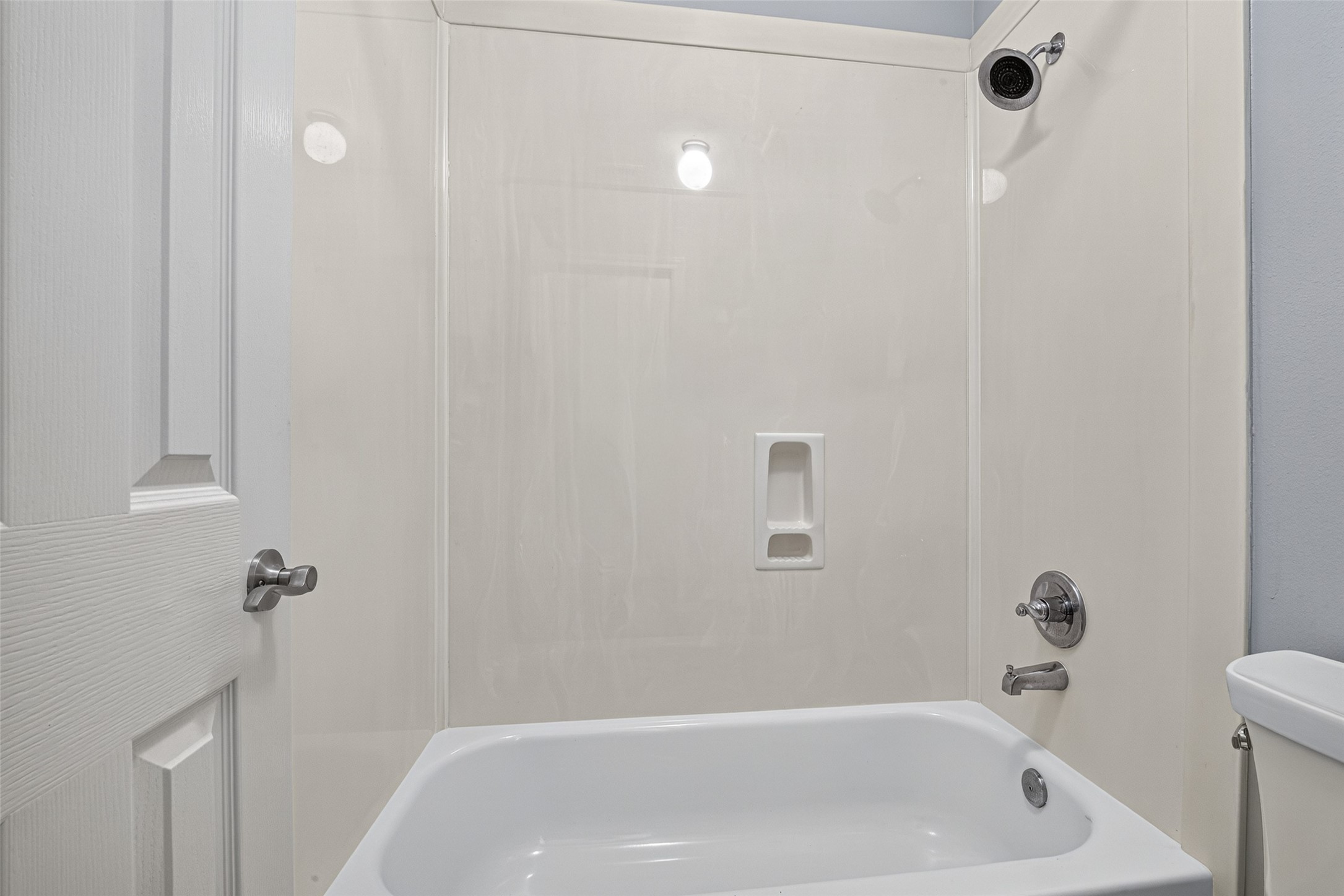 Secondary bathroom includes a tub-and-shower combination with a white surround, built-in toiletry recesses, and chrome-tone fixtures. bathroom
