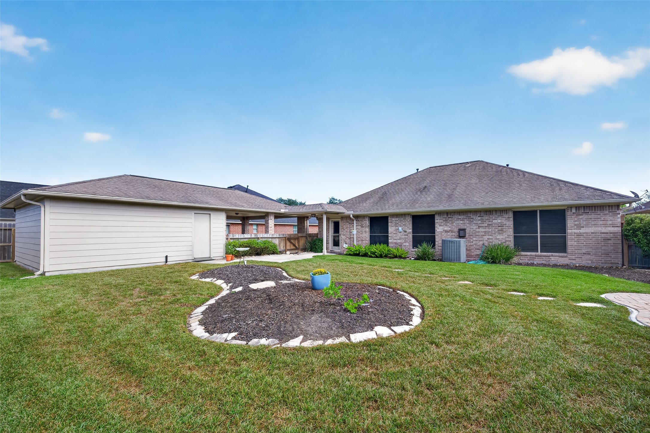 Broad backyard view features a central landscaped bed with stone edging, open lawn, wood fencing, and the detached garage.