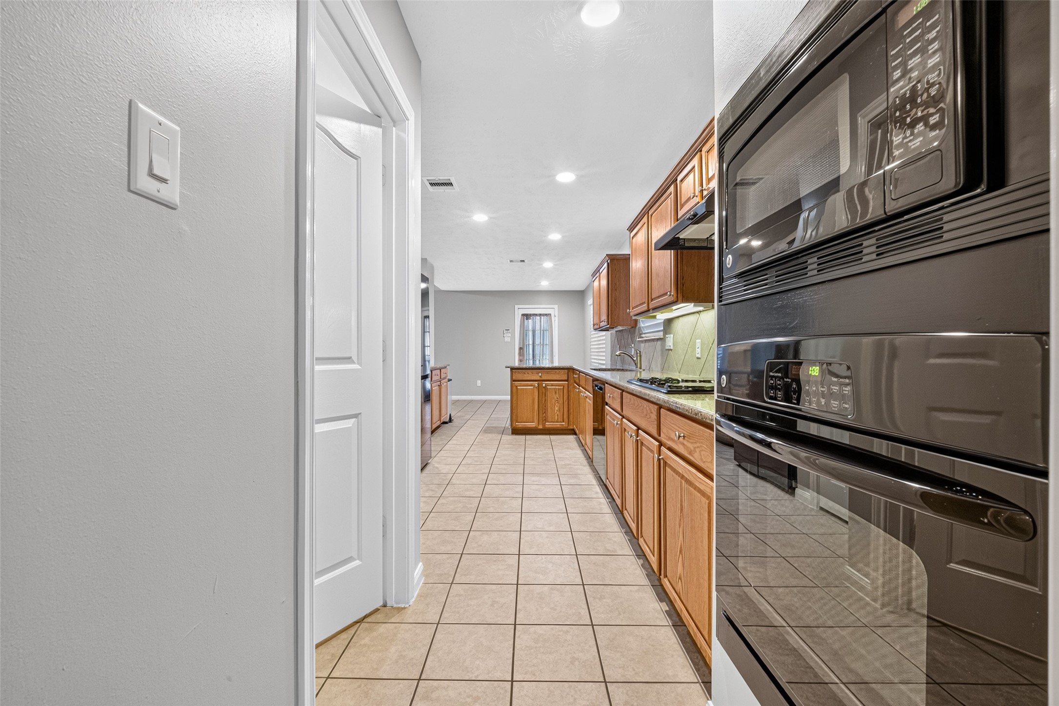 Kitchen view highlights the built-in microwave and oven, tile flooring, recessed lighting, and an extended run of wood cabinetry.