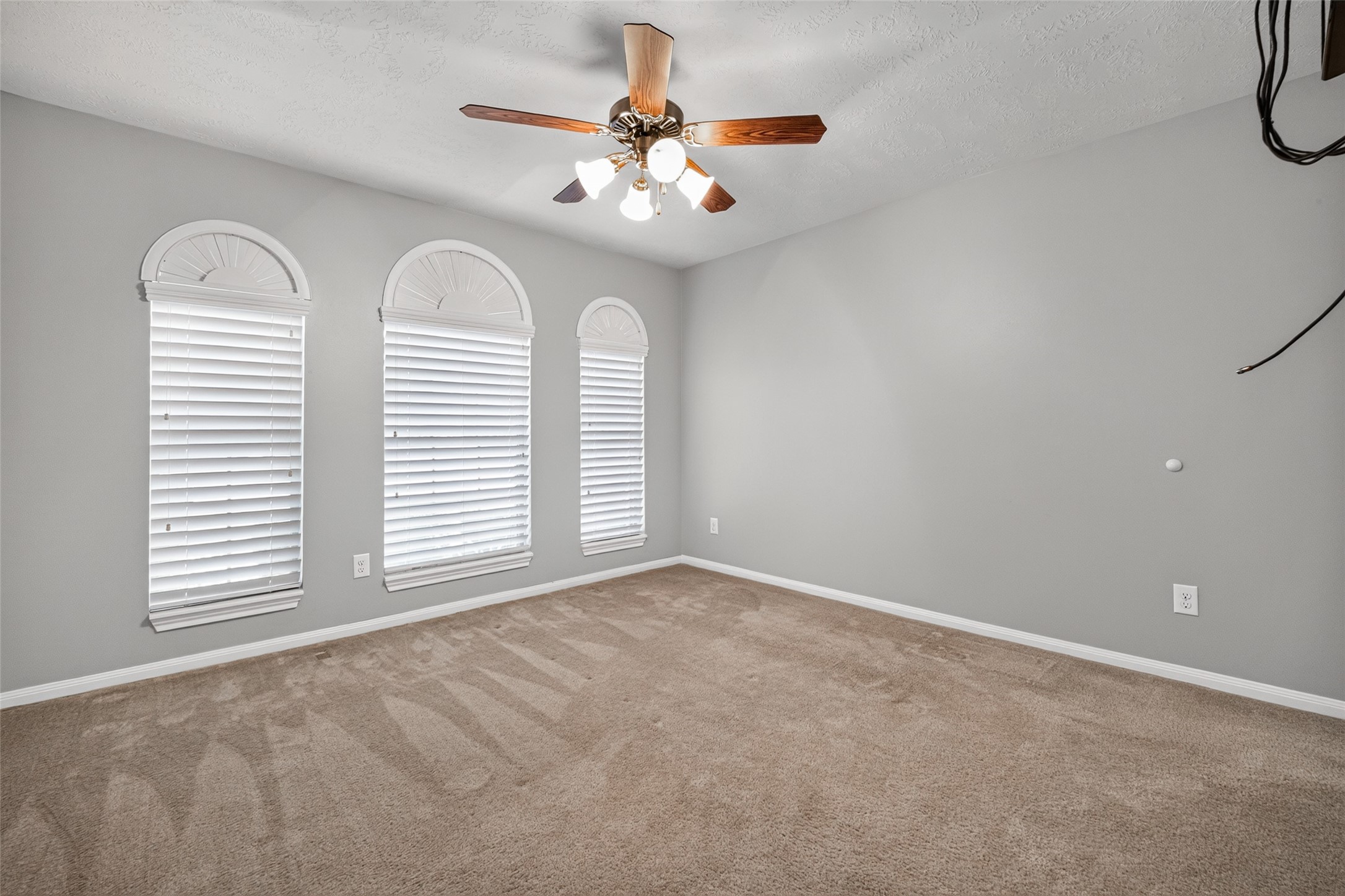 Alternate secondary-bedroom view highlights the trio of arched windows, neutral wall colors, and open floor area.