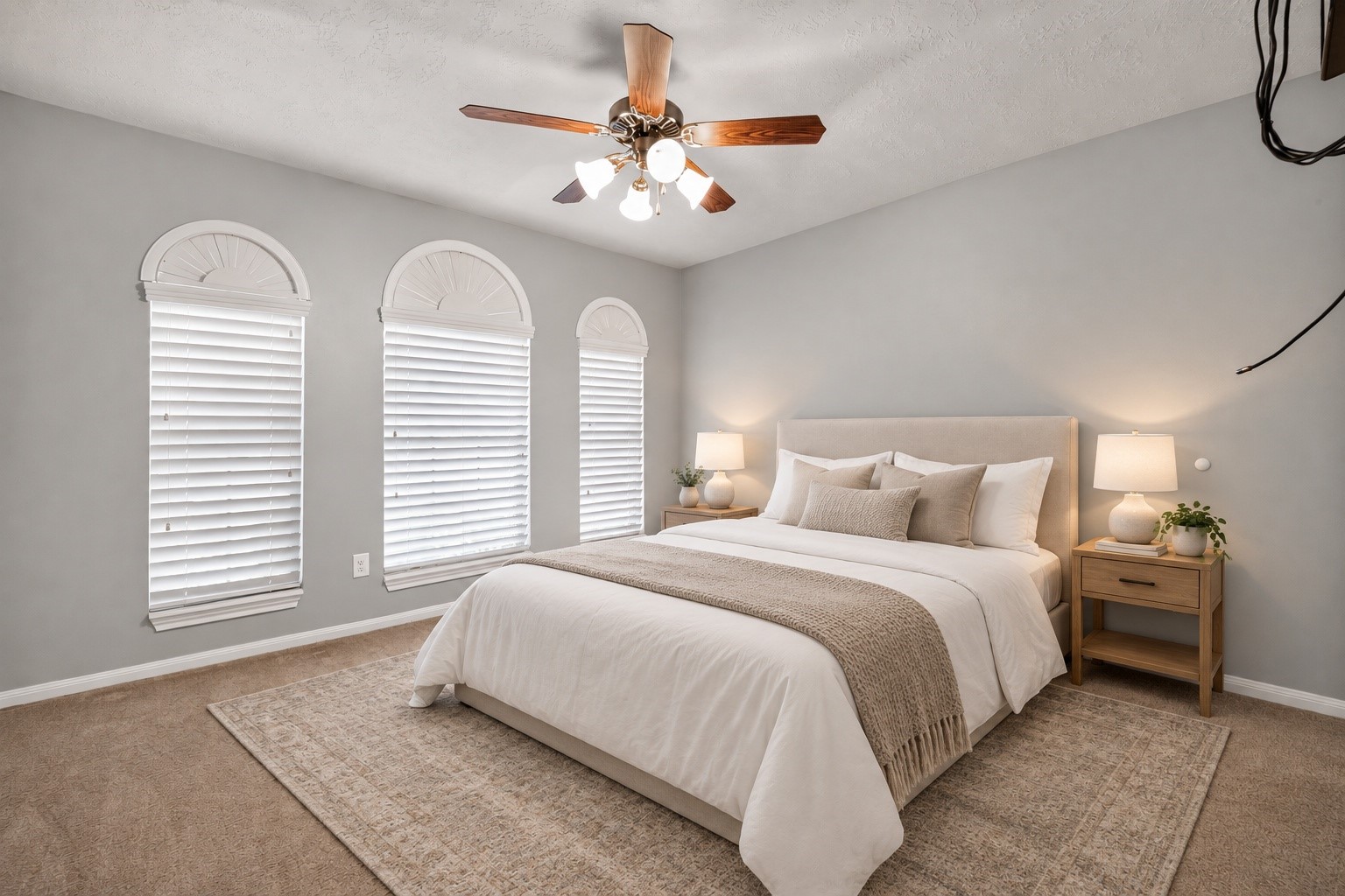 Virtually staged secondary bedroom showcases three arched windows with white blinds, a ceiling fan, neutral walls, and carpeted flooring.