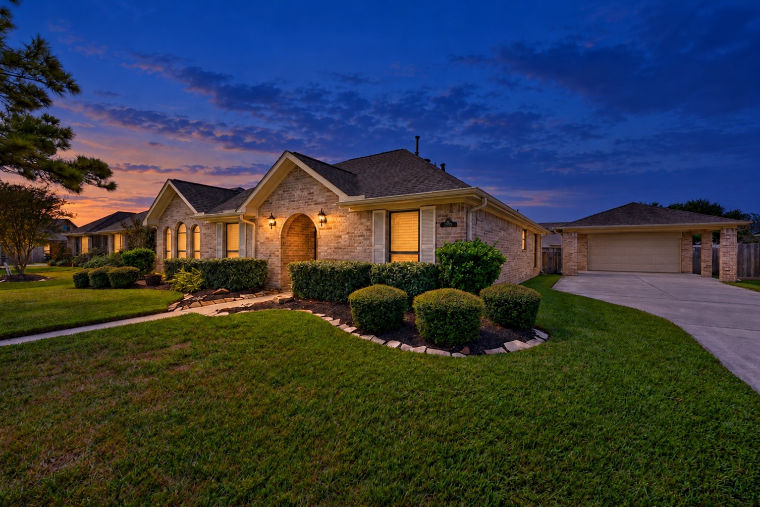 Virtually enhanced twilight photo highlights the brick exterior, arched front entry, landscaped beds, and driveway leading to the detached garage. Virtually enhanced twilight photo highlights the brick exterior, arched front entry, landscaped beds, and driveway leading to the detached garage.
