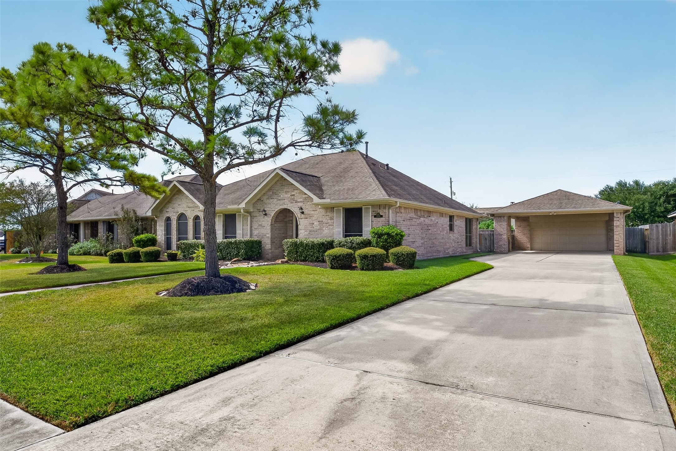 Extended driveway provides access to the detached garage and covered parking area, with mature trees and landscaping framing the home.