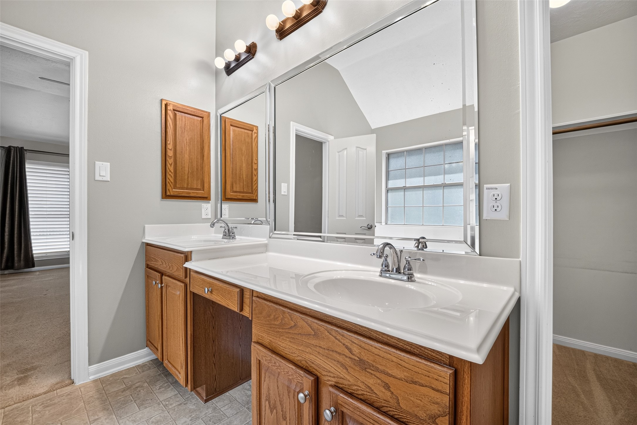 Extended primary-bathroom vanity provides two sinks, drawer and cabinet storage, and a central knee-space area beneath large mirrors.