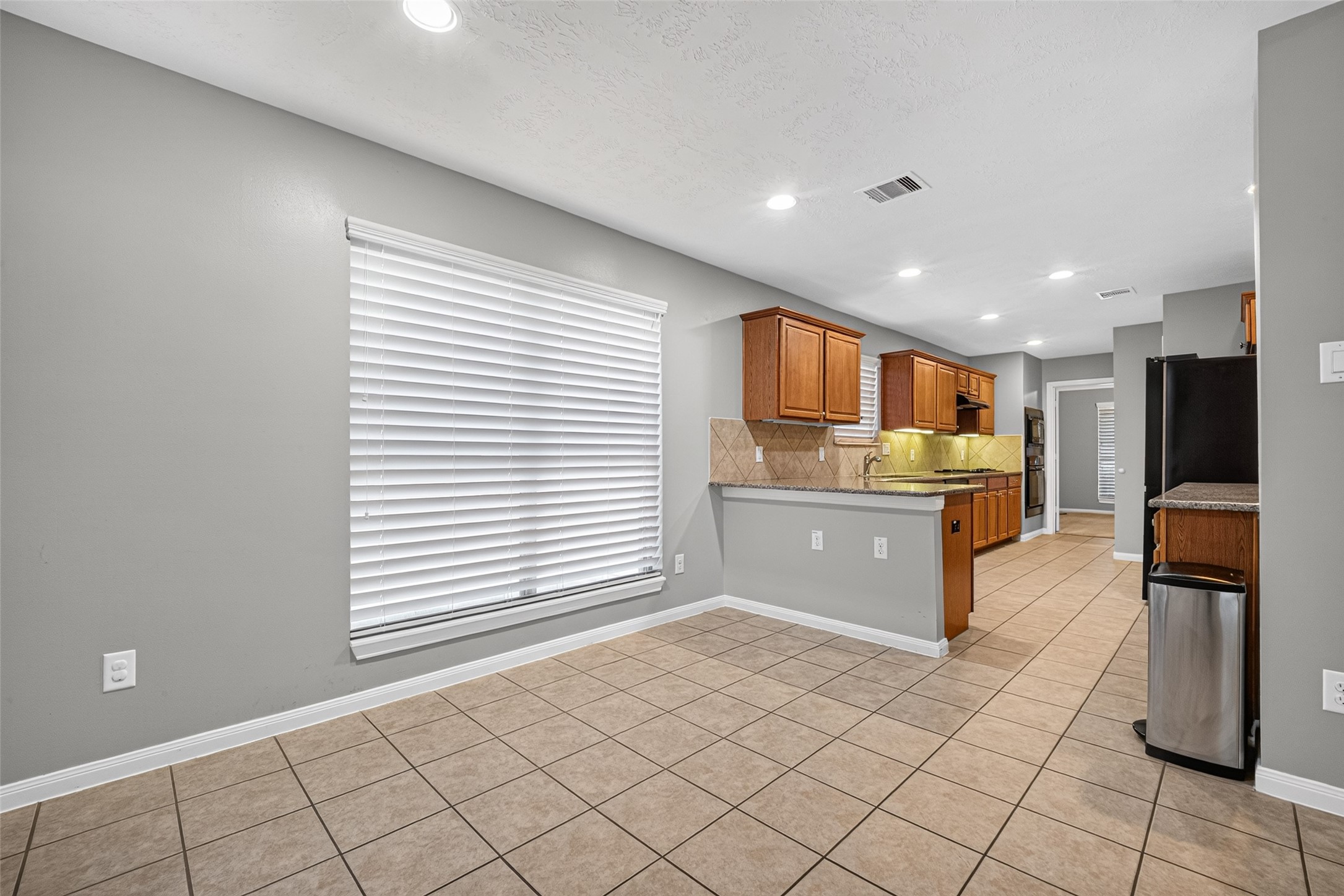 Breakfast area offers tile flooring, a large window with white blinds, and an open connection to the kitchen and counter.