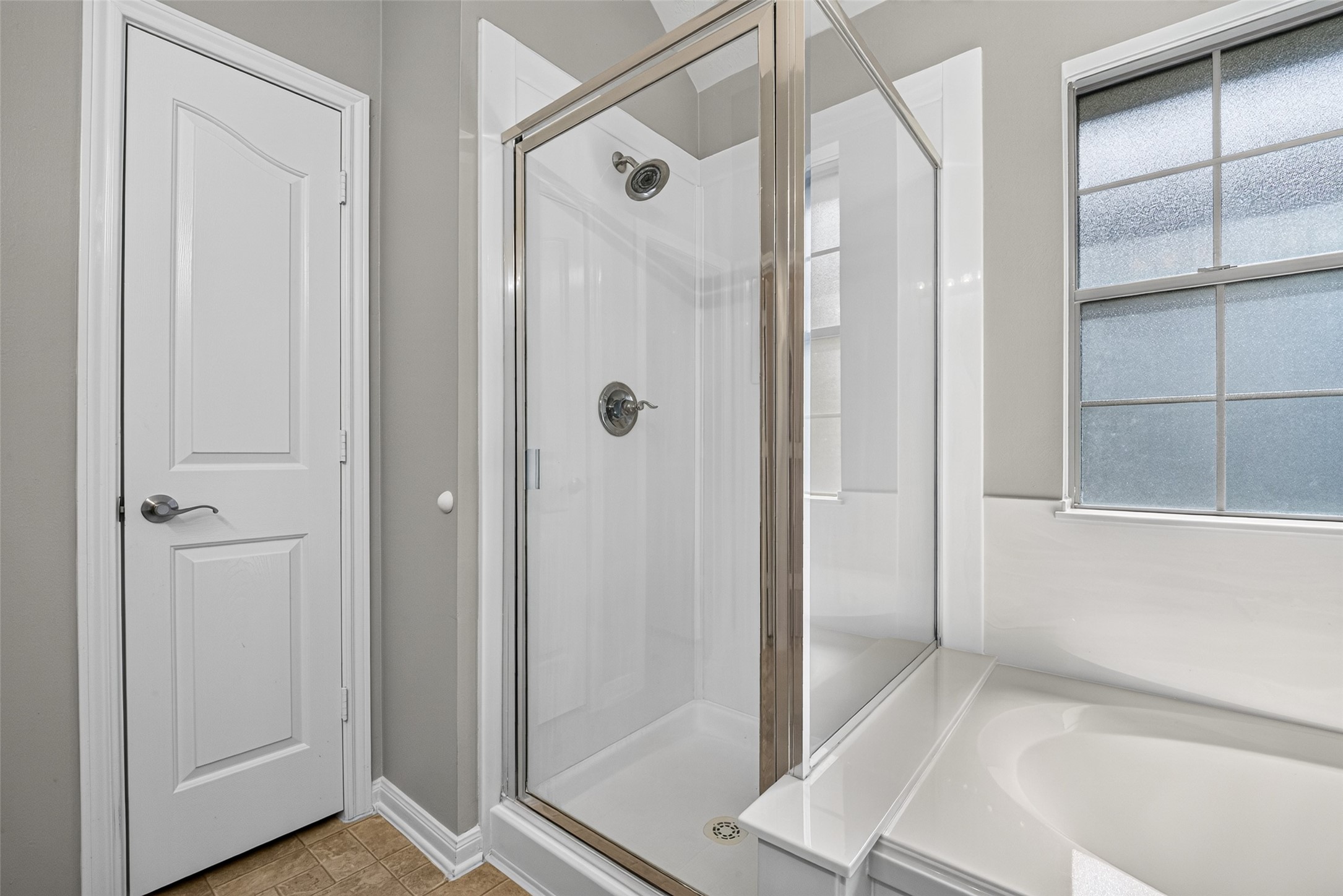 Closer view of the primary bathing area highlights the separate shower enclosure, adjacent tub, and window above the tub surround.