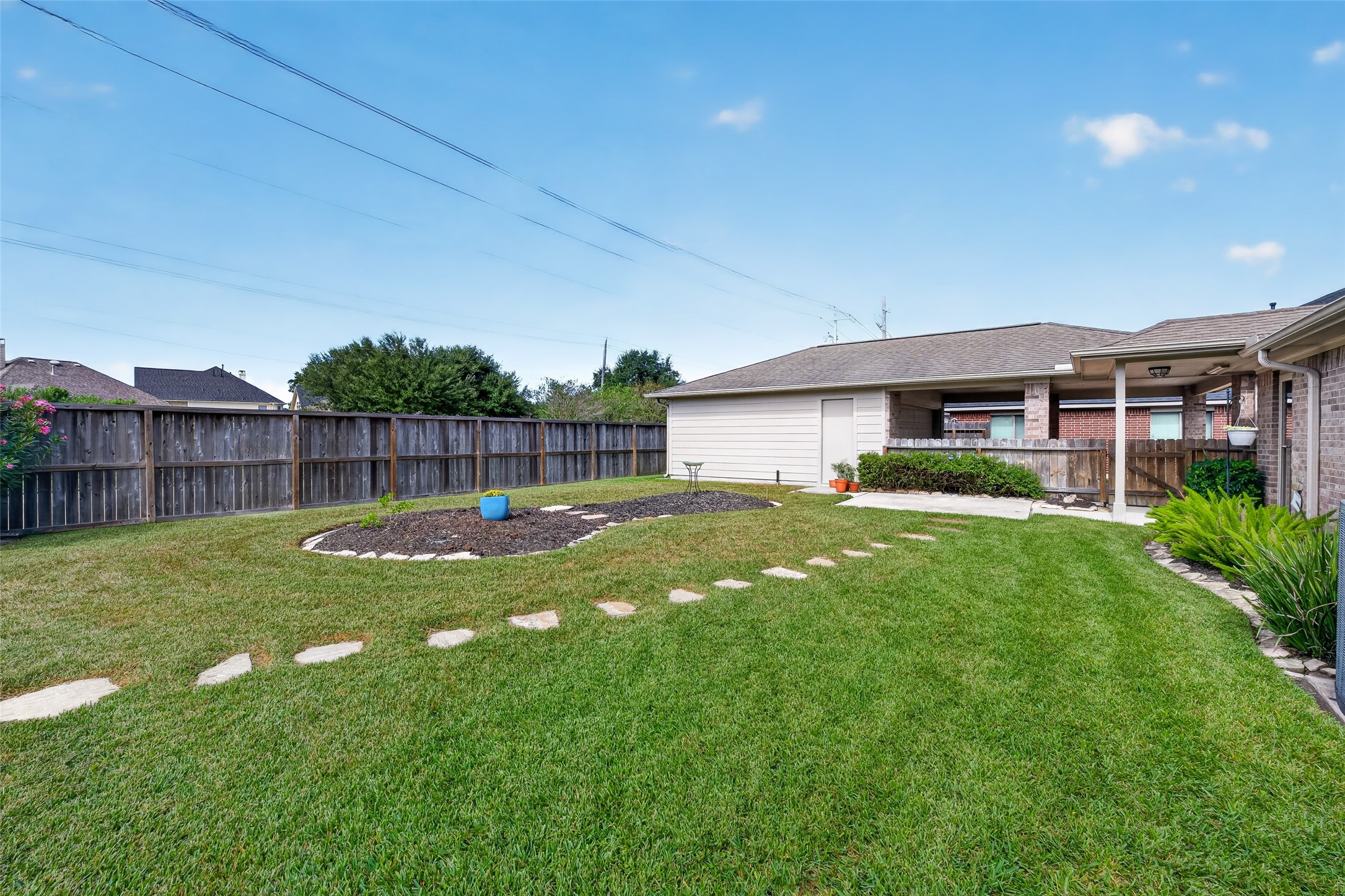 Backyard view showcases an open lawn, curved stepping-stone path, landscaped island bed, and detached garage along the rear boundary.
