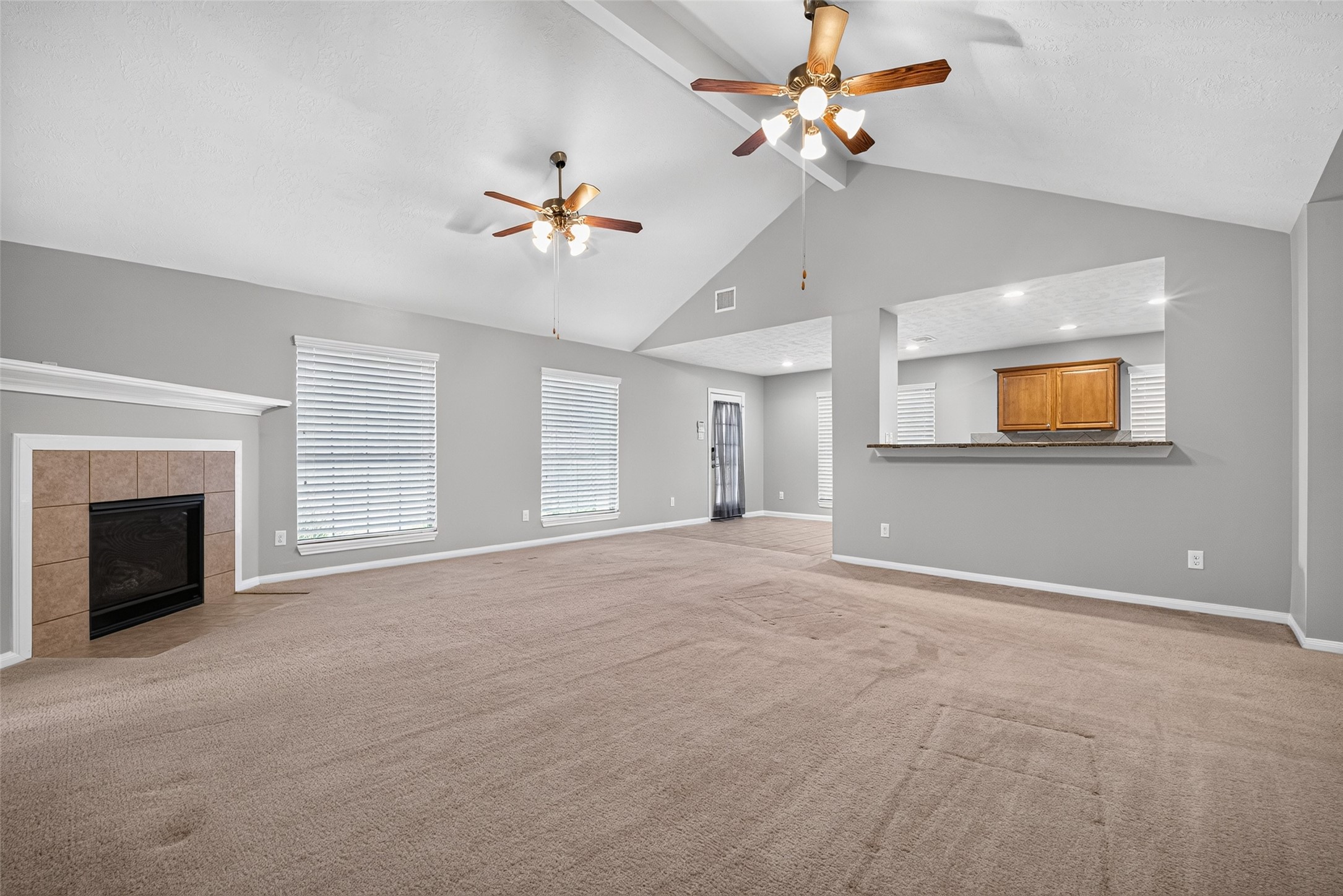 Reverse living-room view showcases the fireplace, multiple windows, and a wide opening to the tile-floored breakfast and kitchen areas.