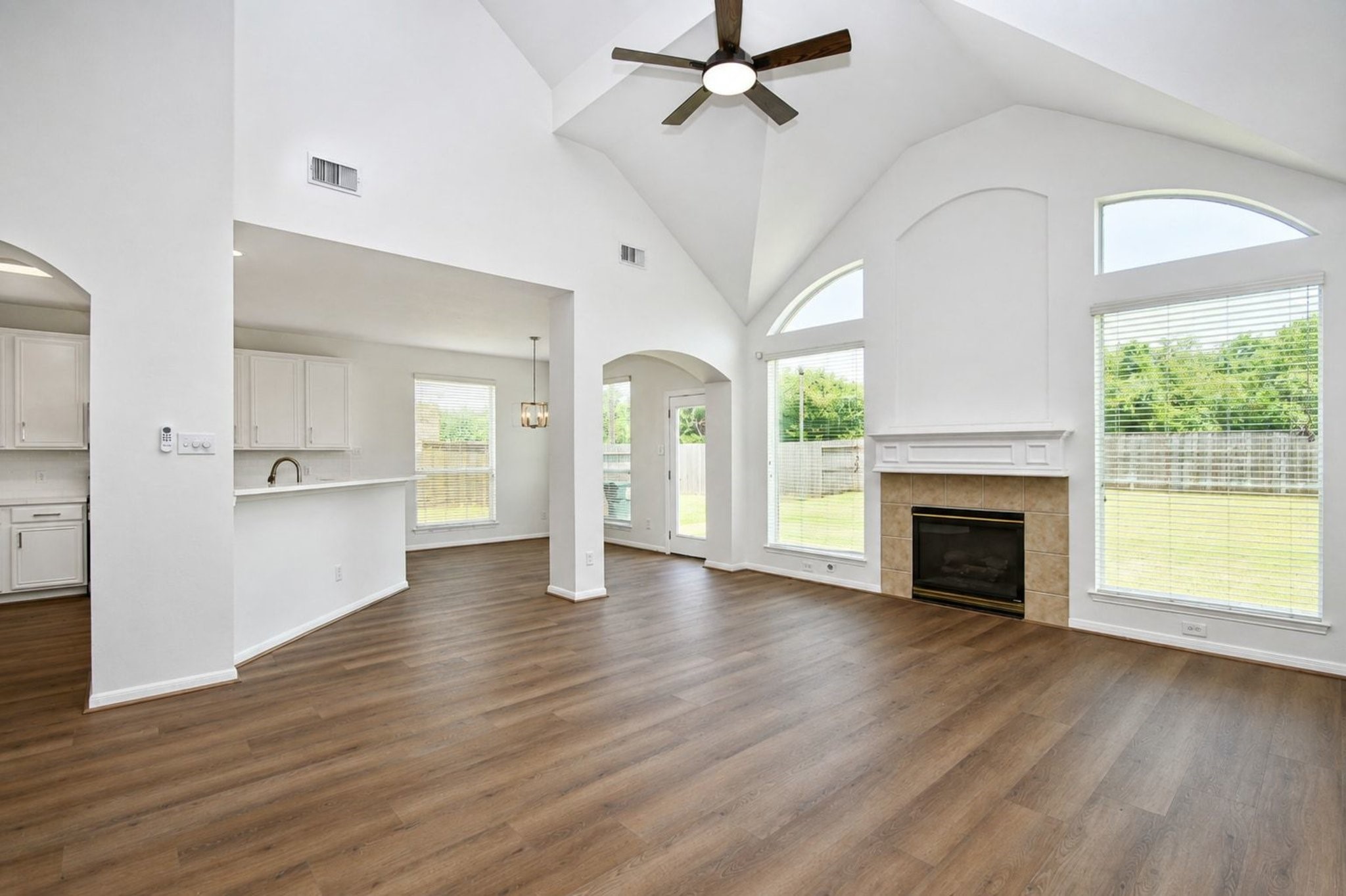 Stunning open-concept living space with vaulted ceilings, large windows for natural light, and a cozy fireplace, seamlessly flowing into a bright kitchen area.