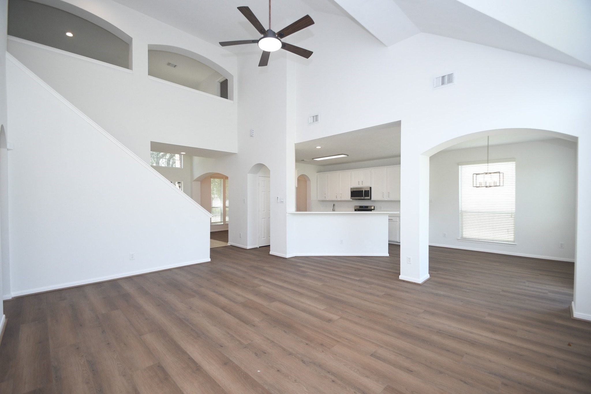 Spacious open-concept living area with high ceilings, elegant wood flooring, and abundant natural light, seamlessly connected to a modern kitchen with white cabinetry and stainless steel appliances.