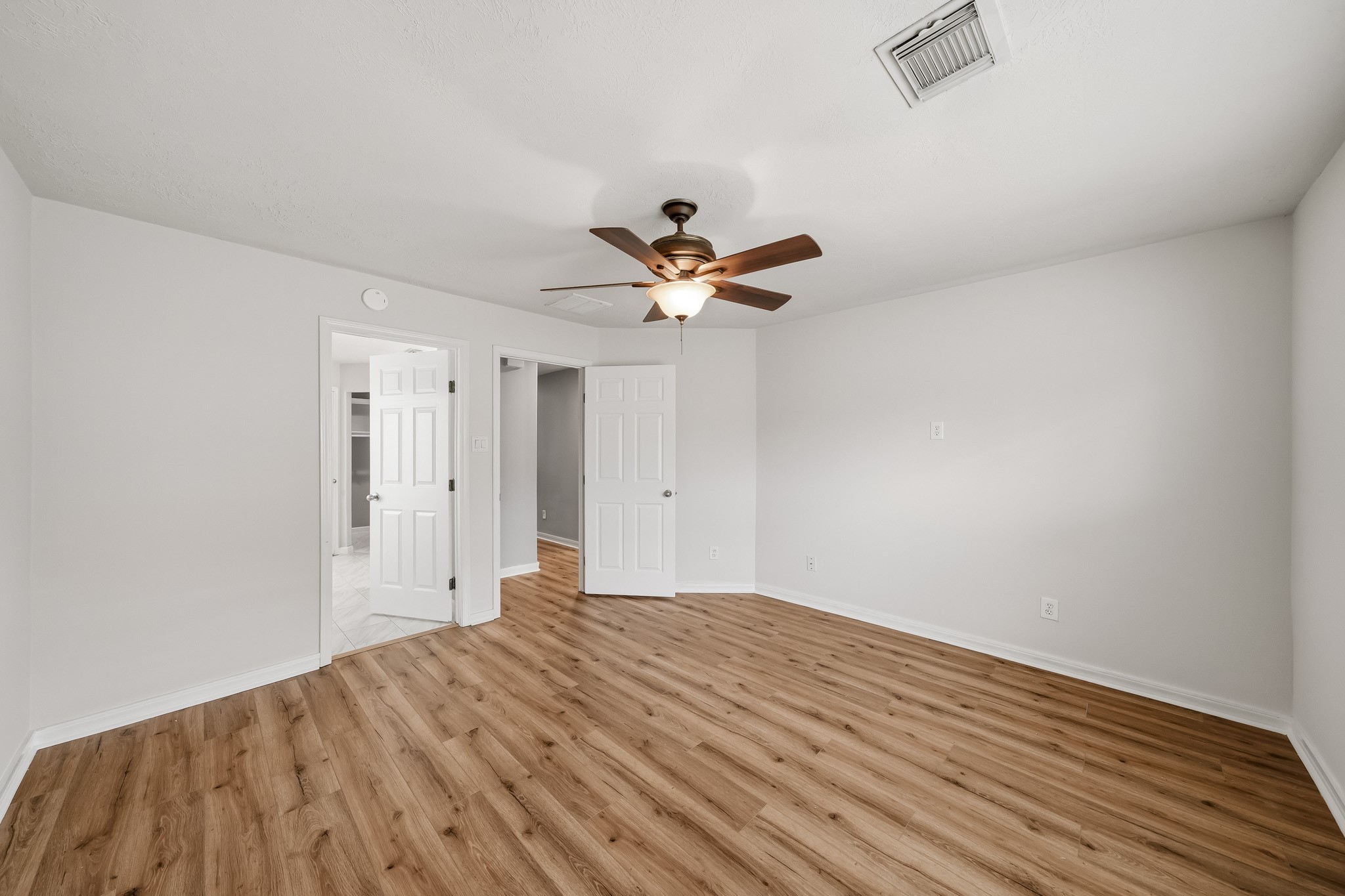 Spacious primary bedroom features warm flooring, neutral finishes, and plenty of natural light.