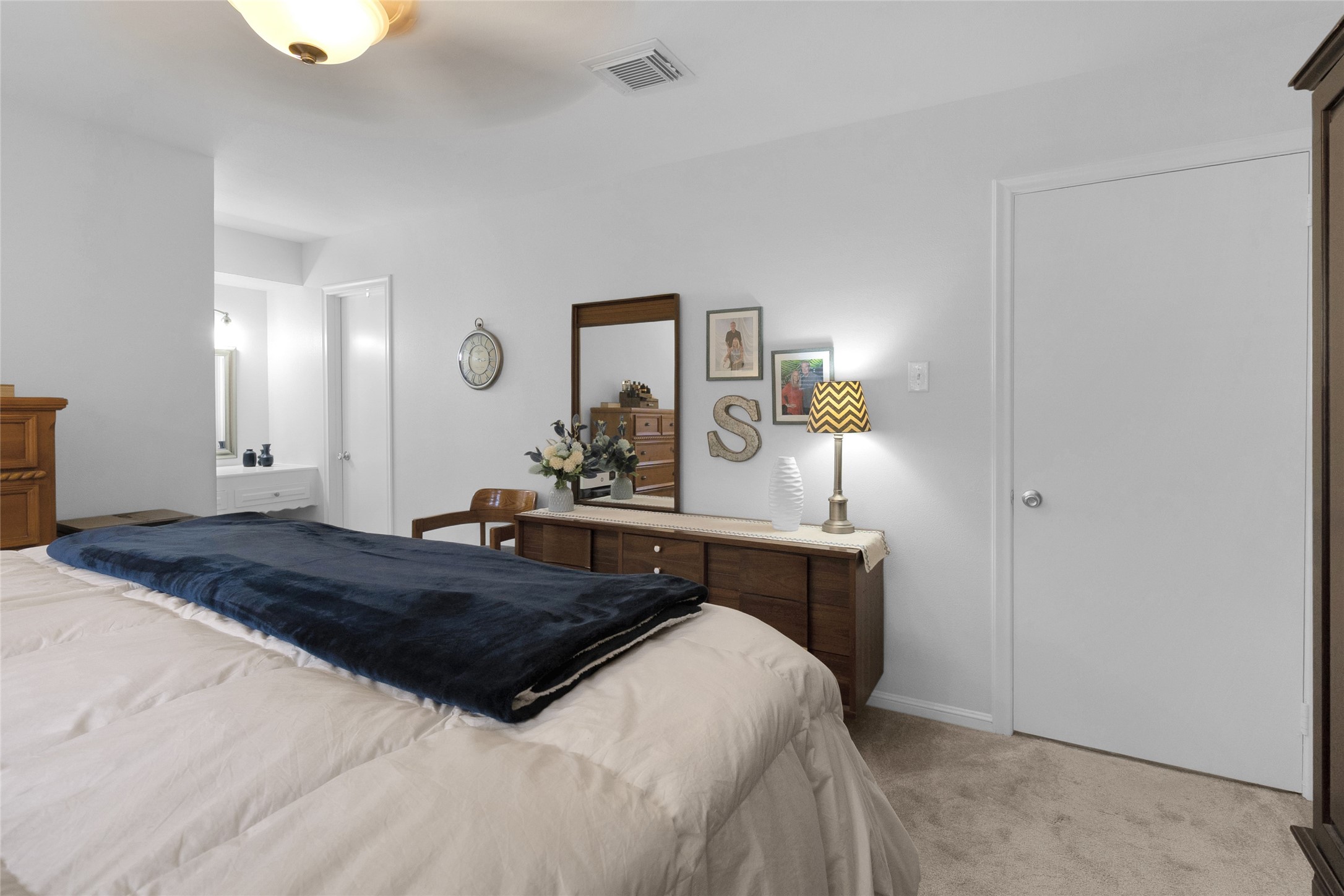 Spacious bedroom with modern decor, featuring a cozy bed, elegant dresser, and convenient access to a well-lit bathroom.
