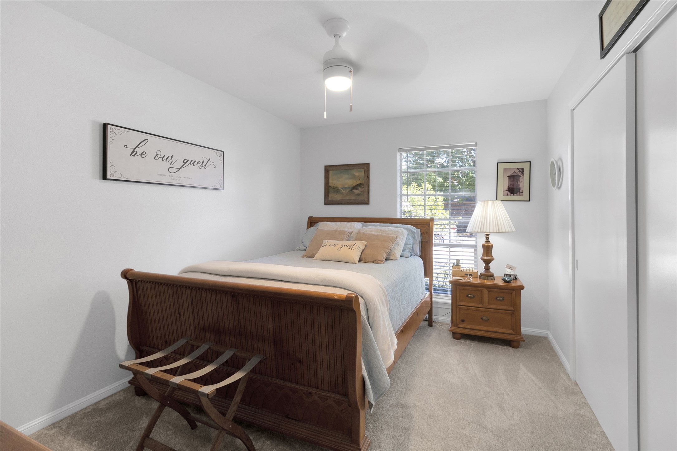 First bedroom with a warm, inviting atmosphere, featuring a wooden bed, plush carpeting, and ample natural light from a large window.