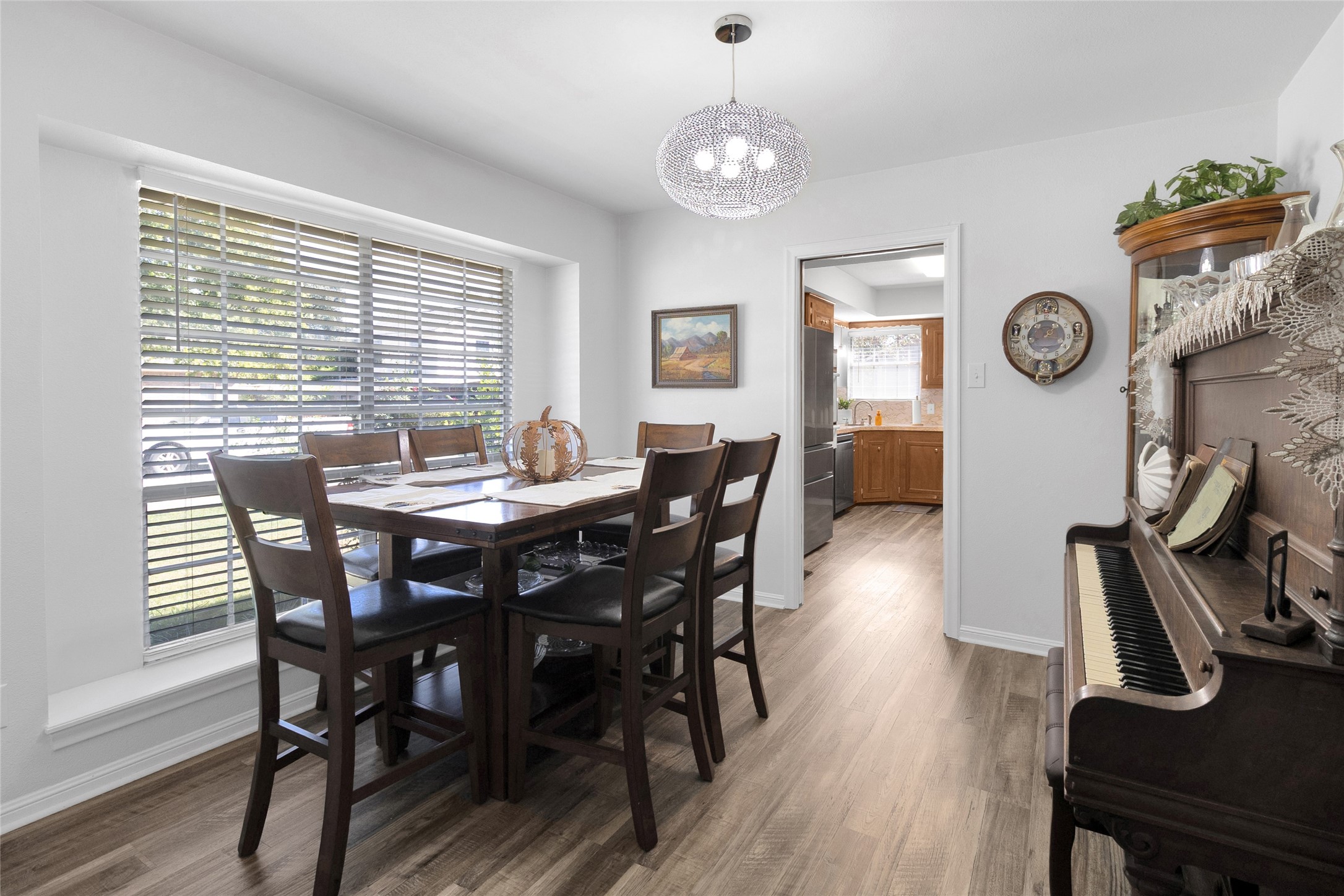Elegant dining area with abundant natural light, featuring a stylish chandelier, cozy piano nook, and seamless access to the adjacent kitchen.