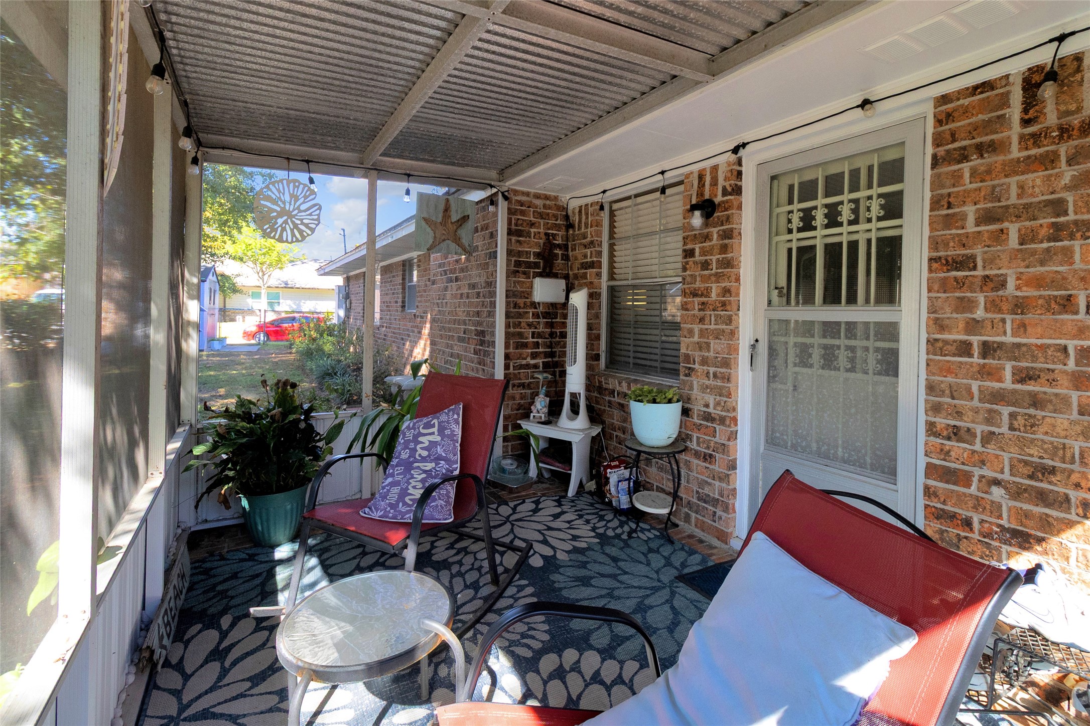 Charming screened-in porch with cozy seating, vibrant plants, and a decorative rug, perfect for relaxing outdoors.
