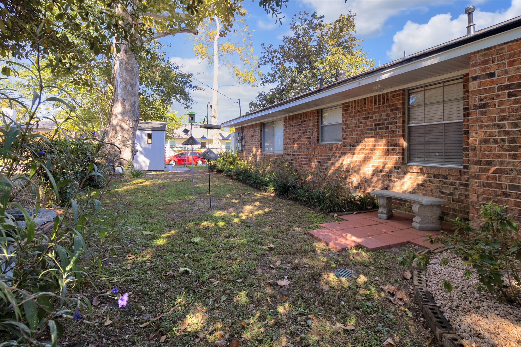 Backyard oasis with mature trees, lush landscaping, and a cozy brick patio perfect for relaxing outdoors.